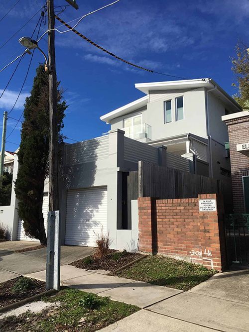 A White House With a Brick Wall and a White Garage Door — Dowdy Constructions in Forster, NSW