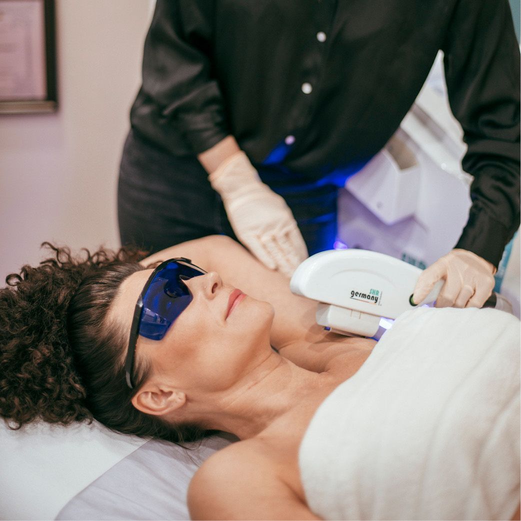 Eine Frau mit Sonnenbrille bekommt eine Laserbehandlung am Hals