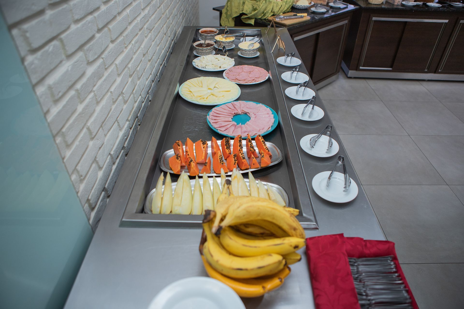 Buffet com diversos itens alimentícios em exposição, incluindo presunto, queijo e frutas.