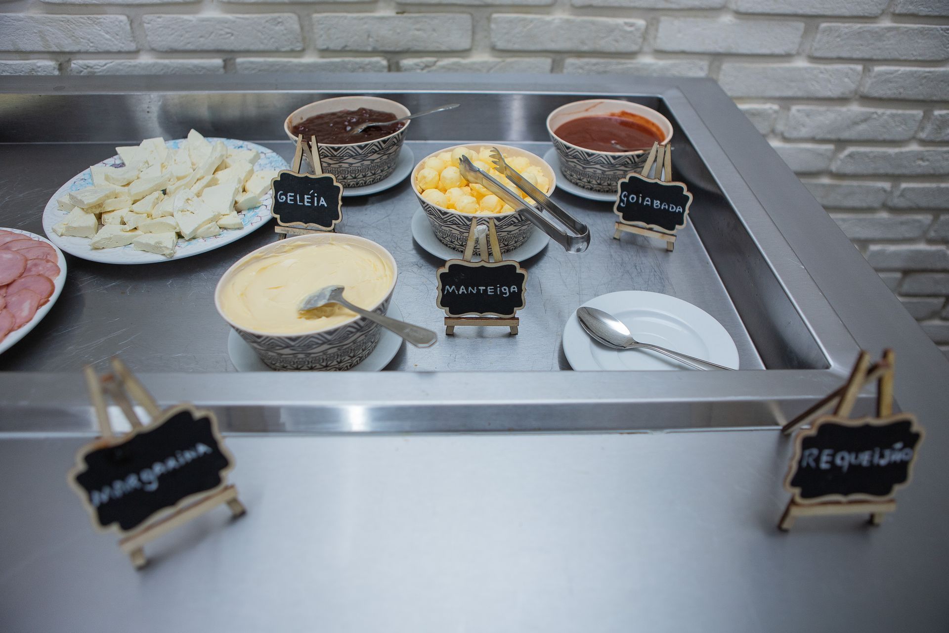 Buffet com diversas opções de recheios: queijos, molhos e guarnições em uma estação de serviço de metal.