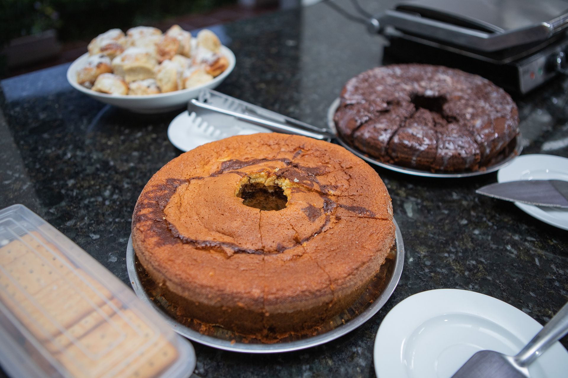 Bolo, pãezinhos e uma chapa sobre uma bancada escura com pintas.