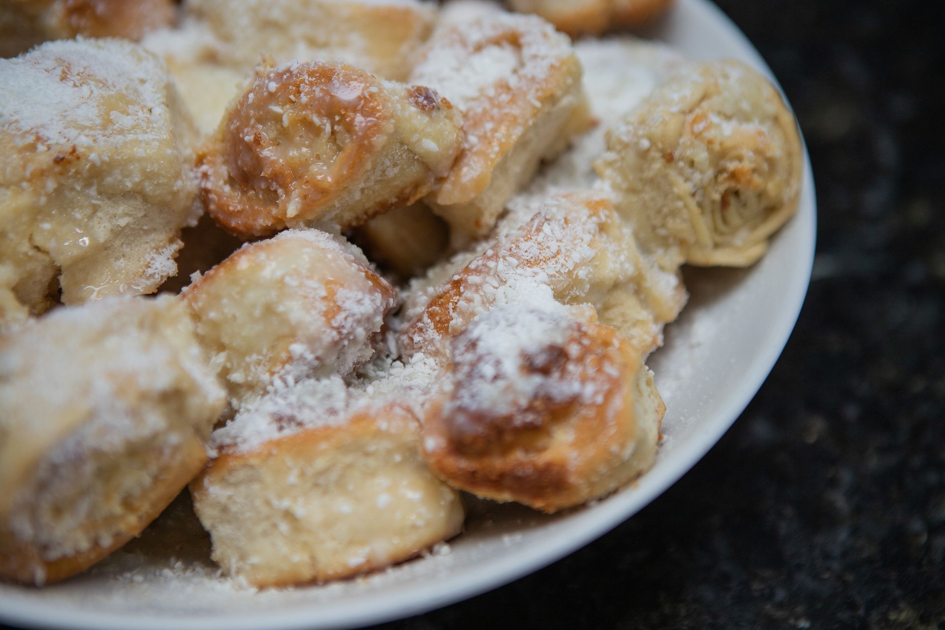 Imagem em close-up de um prato branco repleto de pãezinhos dourados, açucarados e assados.