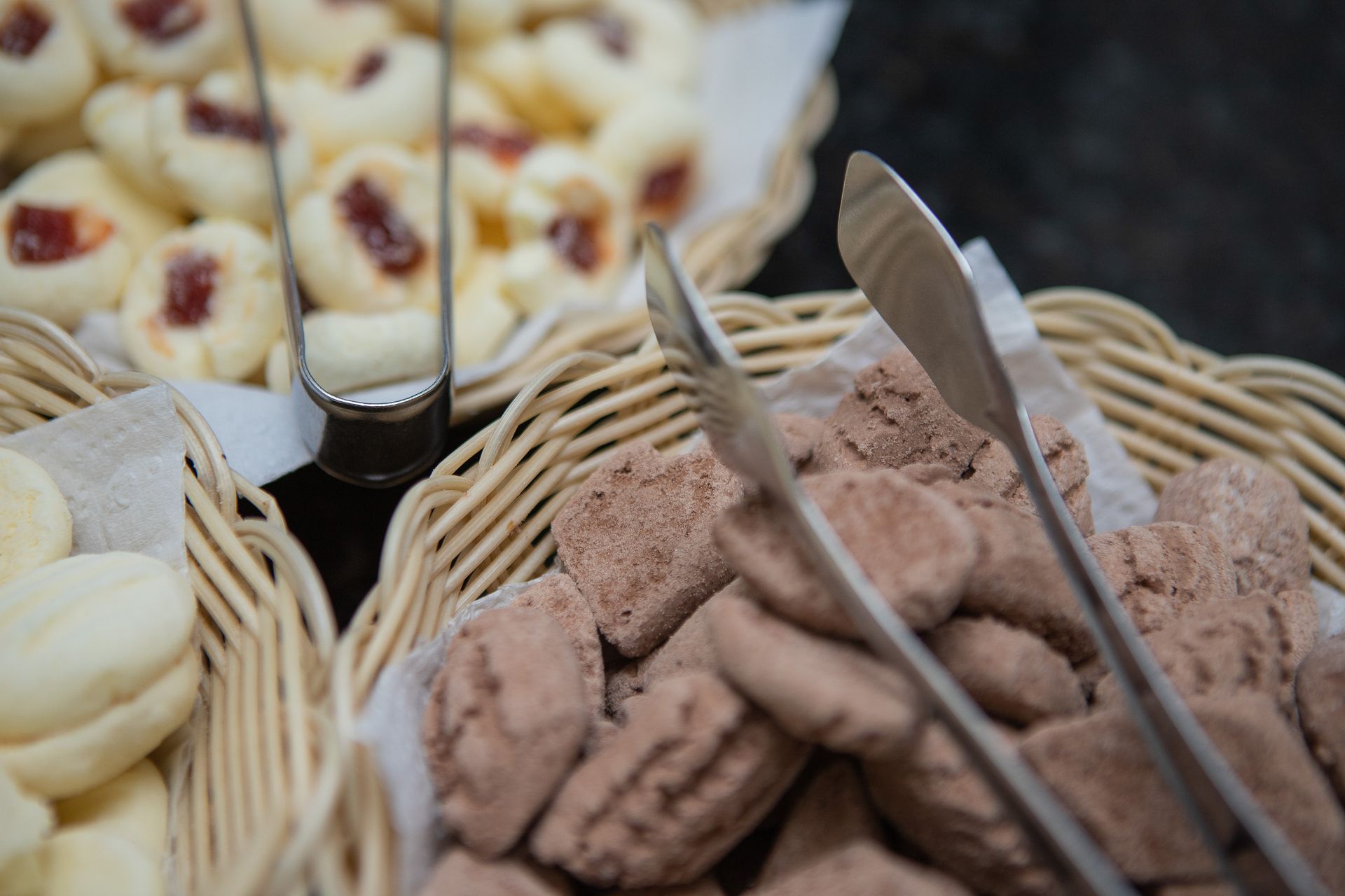 Biscoitos em cestas de vime, com pinças; alguns com cobertura de geleia vermelha, outros de chocolate.