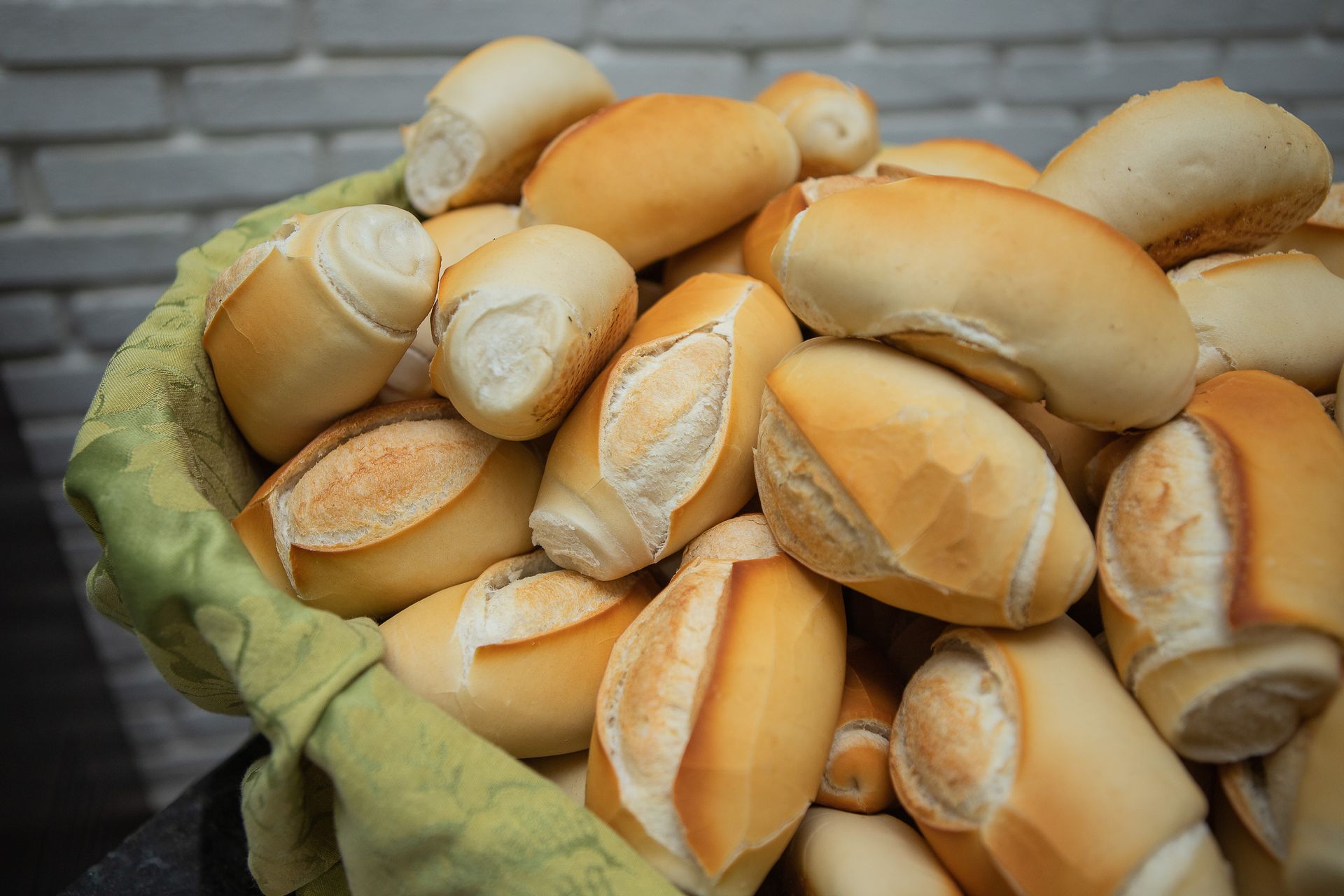 Cesta de pãezinhos brasileiros dourados e crocantes encostada em uma parede de tijolos.