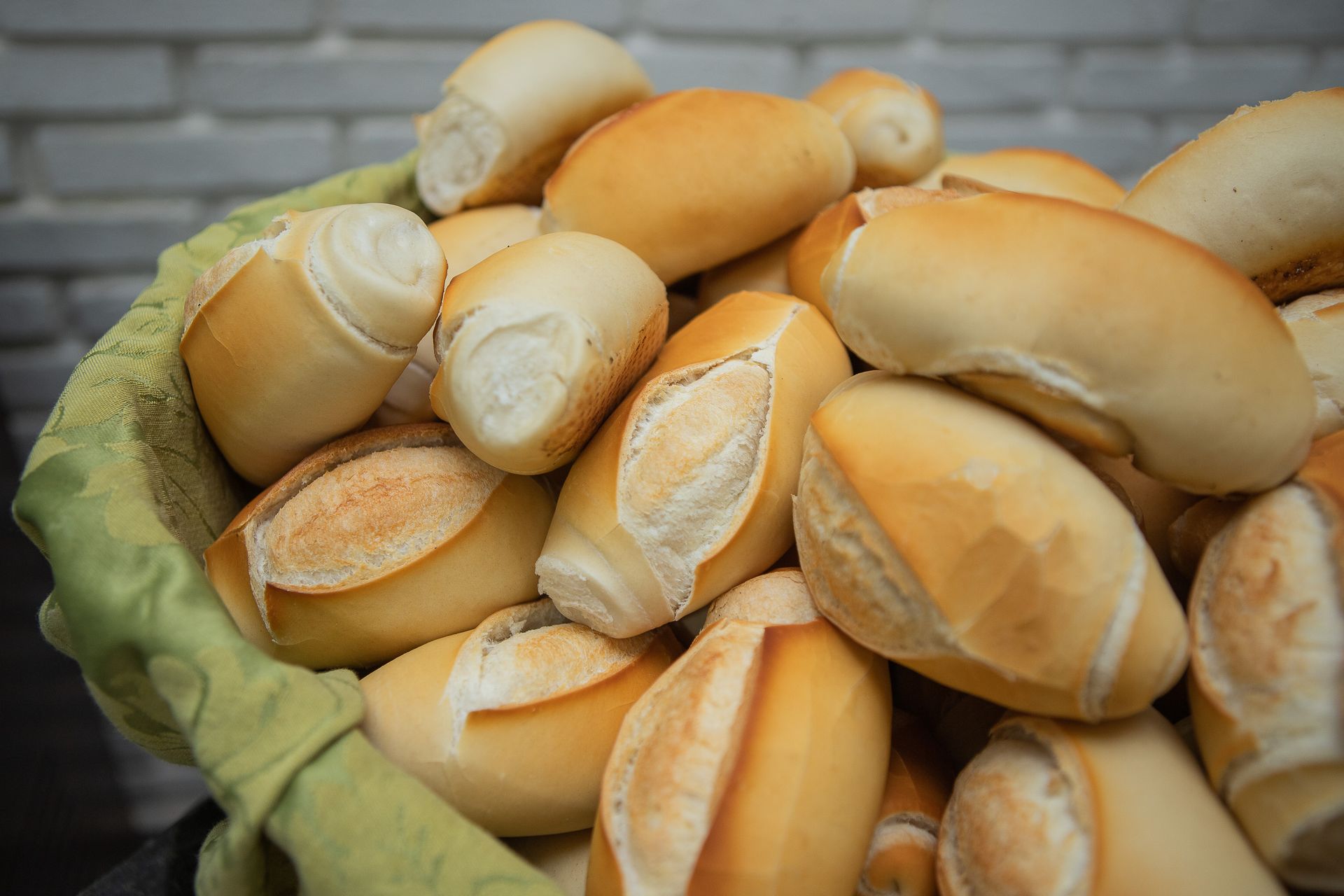 Cesta transbordando de pãezinhos dourados e crocantes encostada em uma parede de tijolos cinza.