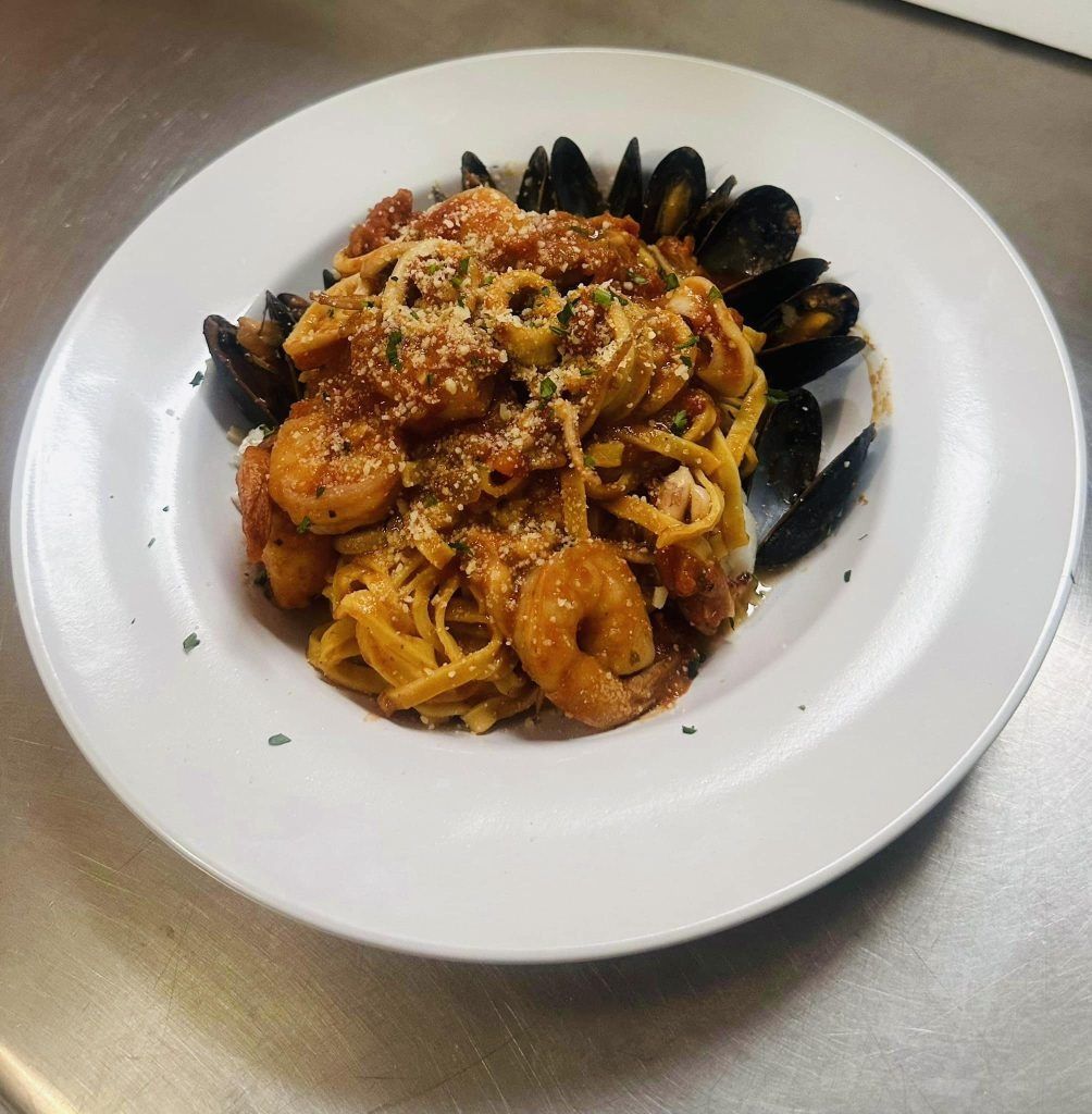 Pasta dish with shrimp, squid, mussels, and tomato sauce, garnished with Parmesan cheese, on a white plate.