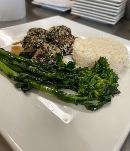 Sesame-crusted fish with rice and broccolini on a white plate.