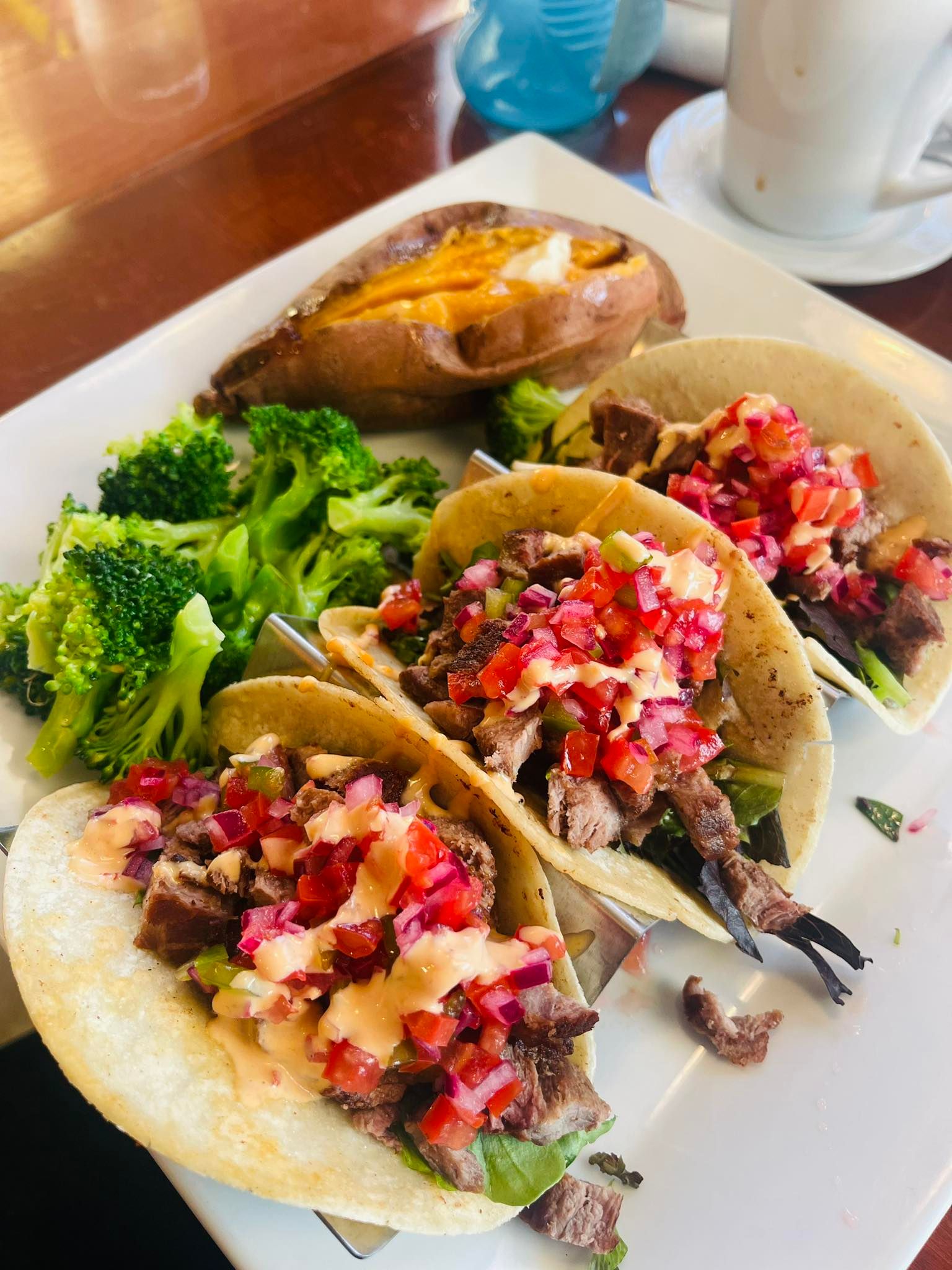 Plate with tacos, sweet potato, broccoli. Tacos have red salsa and sauce. Green broccoli and baked sweet potato.