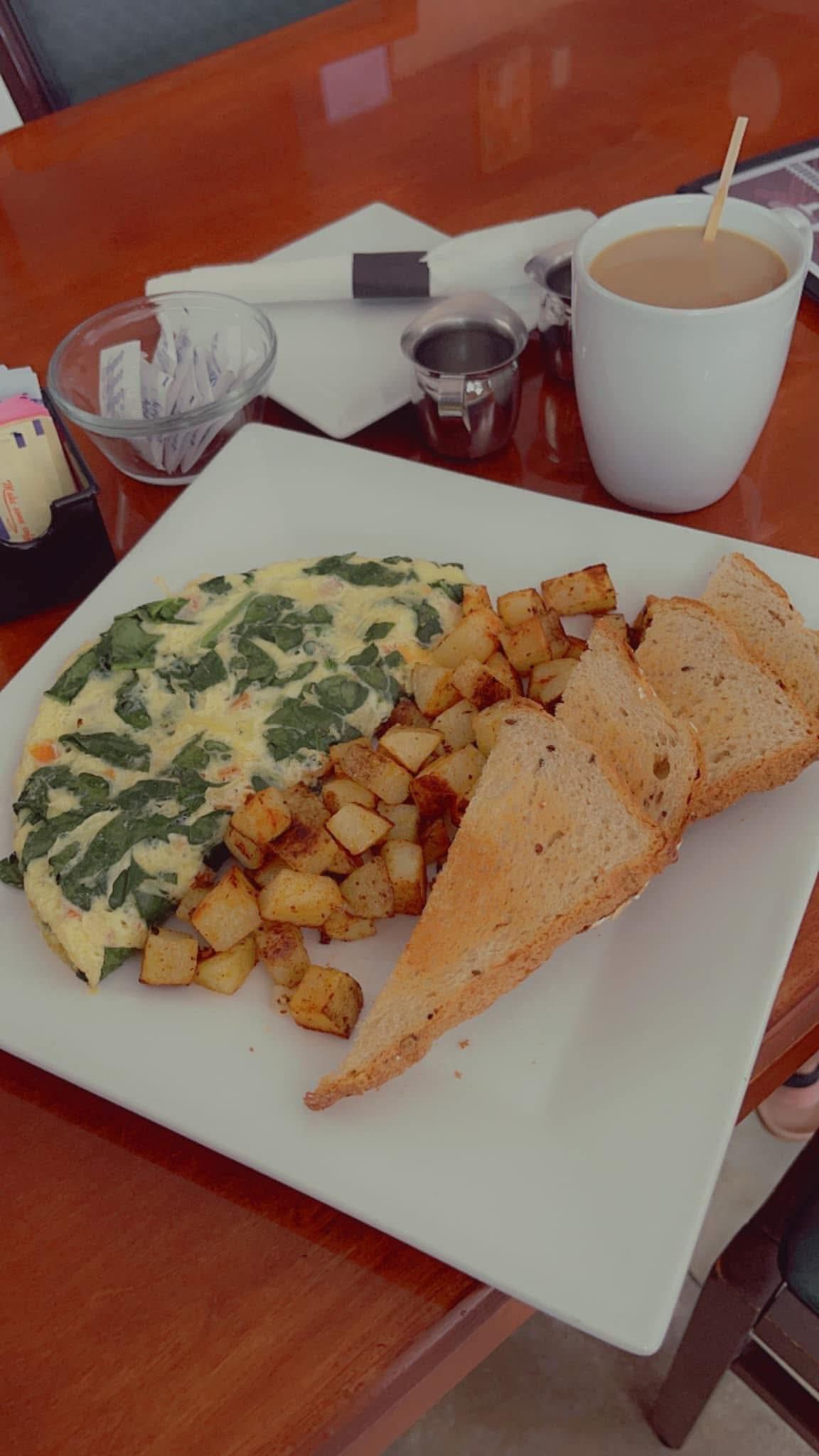 Omelet with potatoes and toast on a plate, coffee, and syrup on a wood table.