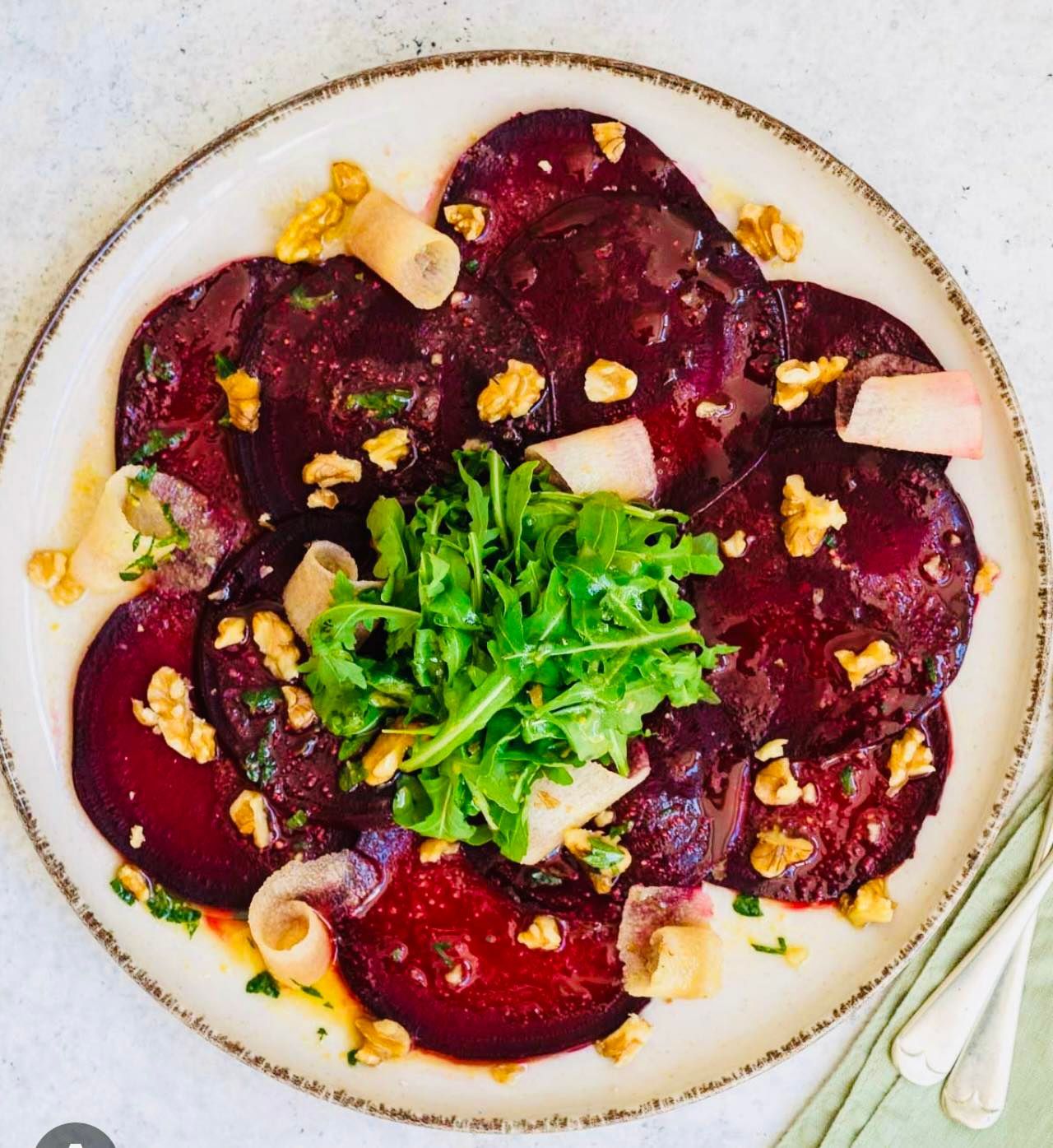 Beet carpaccio with arugula, walnuts, and radish on a white plate.