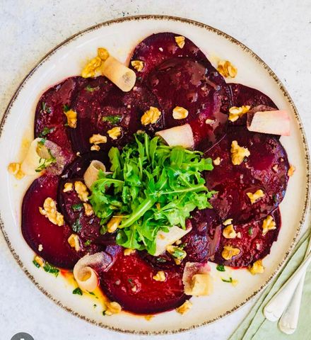 Beet salad with arugula, walnuts, and radish on a white plate.