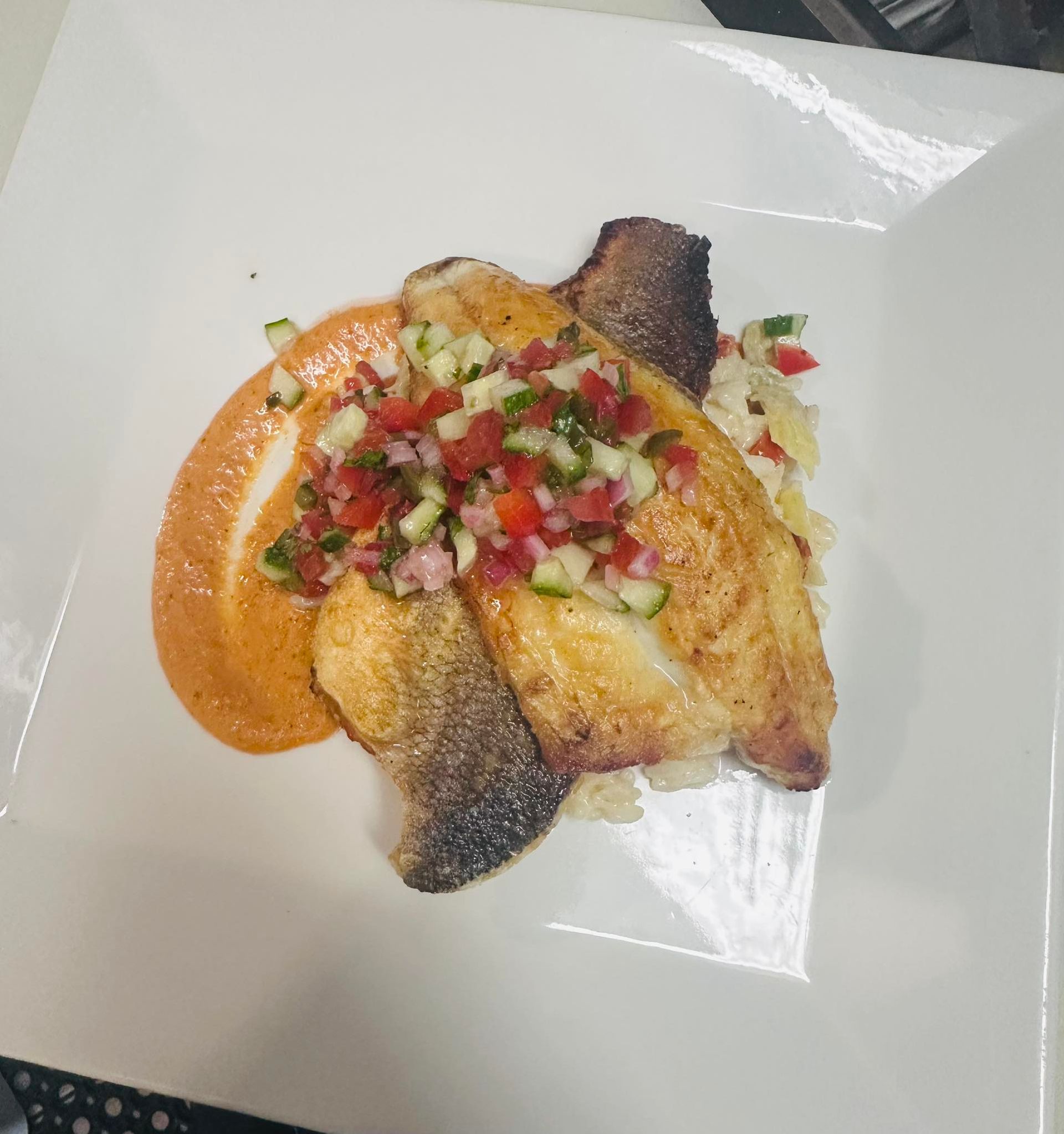 Pan-seared fish with red sauce, salsa, and rice on a white square plate.