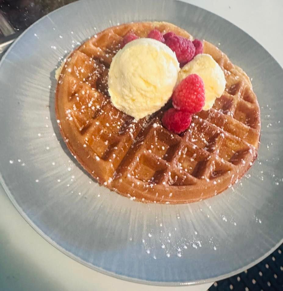 Waffle topped with vanilla ice cream, raspberries, and powdered sugar on a light blue plate.