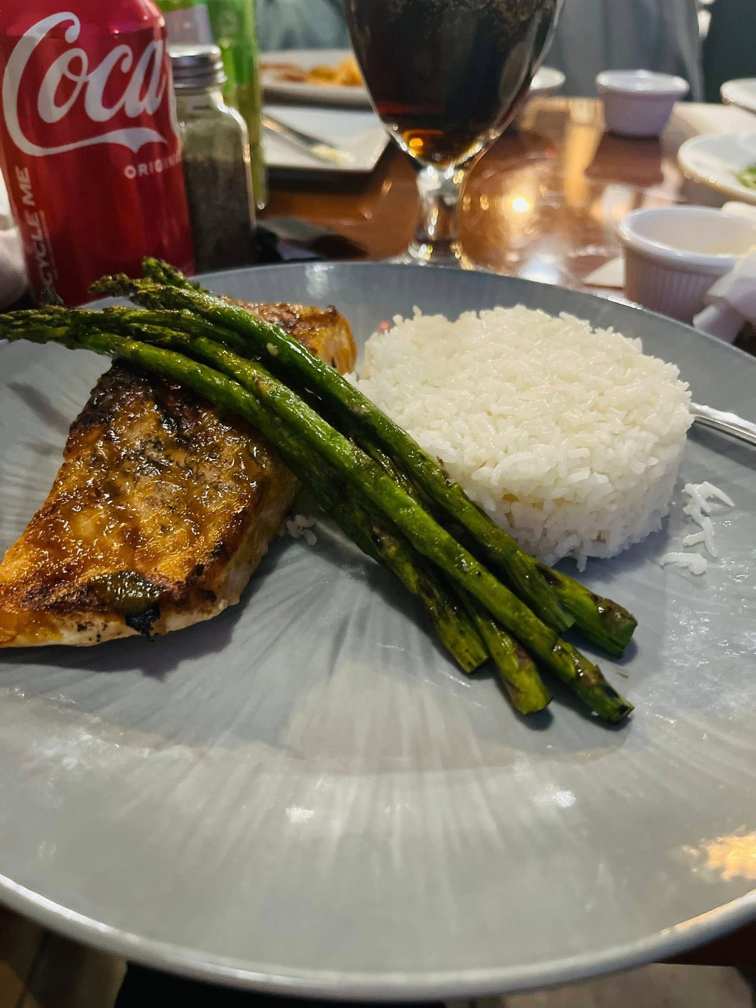 Salmon fillet with asparagus and rice on a plate, alongside a Coca-Cola can and a glass of red wine.