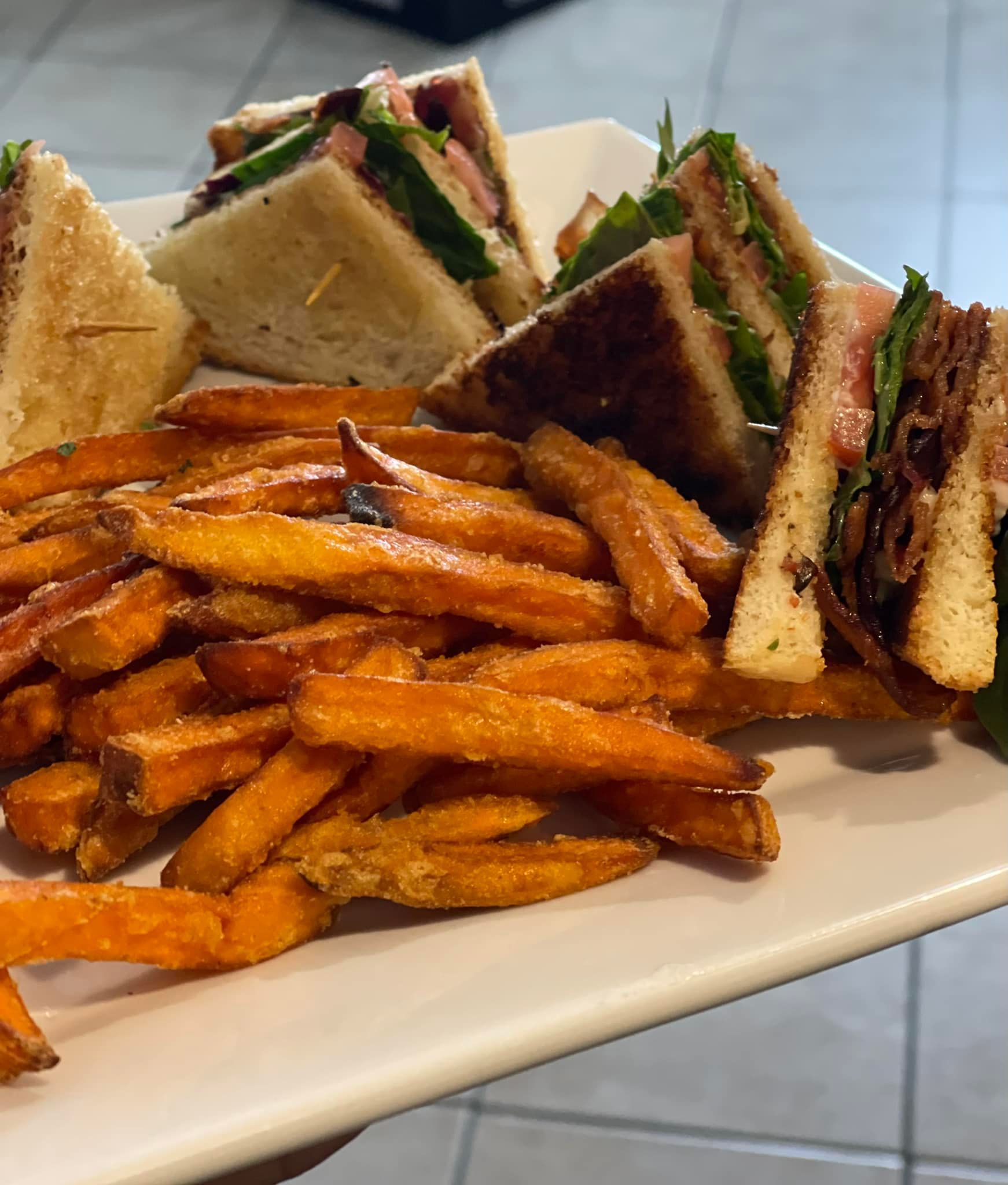 Club sandwich with sweet potato fries on a white plate.
