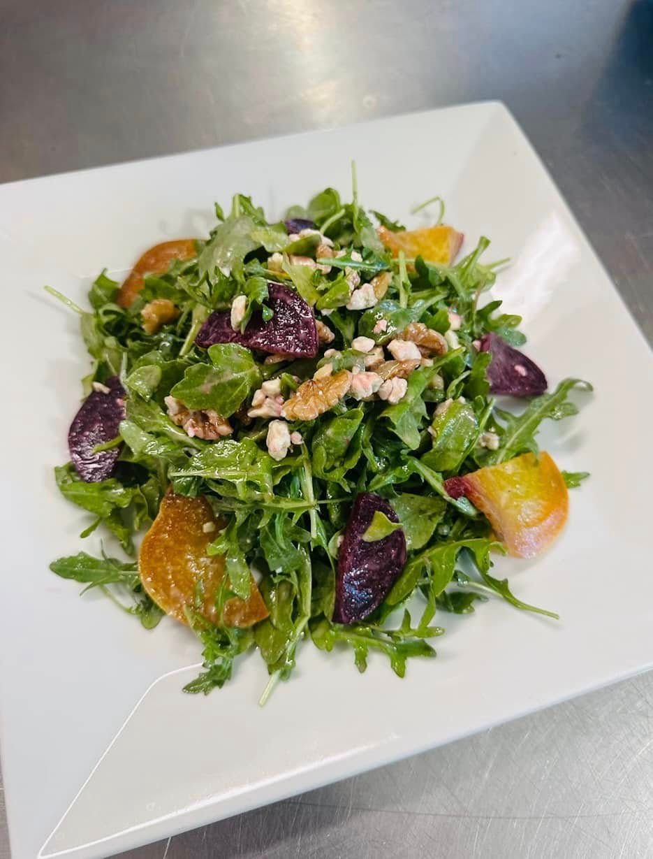 Salad with arugula, roasted beets, peaches, and walnuts on a white square plate.