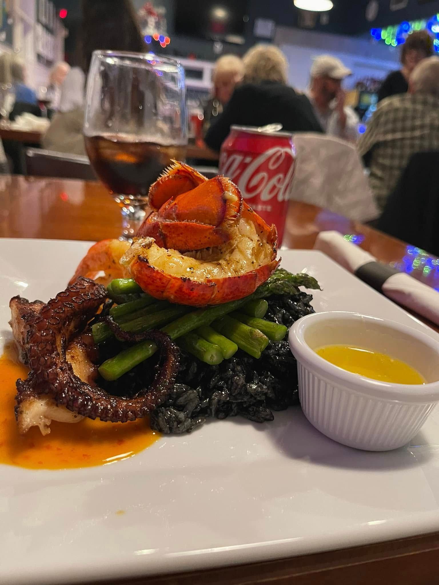 Plate with grilled octopus, lobster, asparagus, and butter, in restaurant. Coca-Cola can and glass of drink.