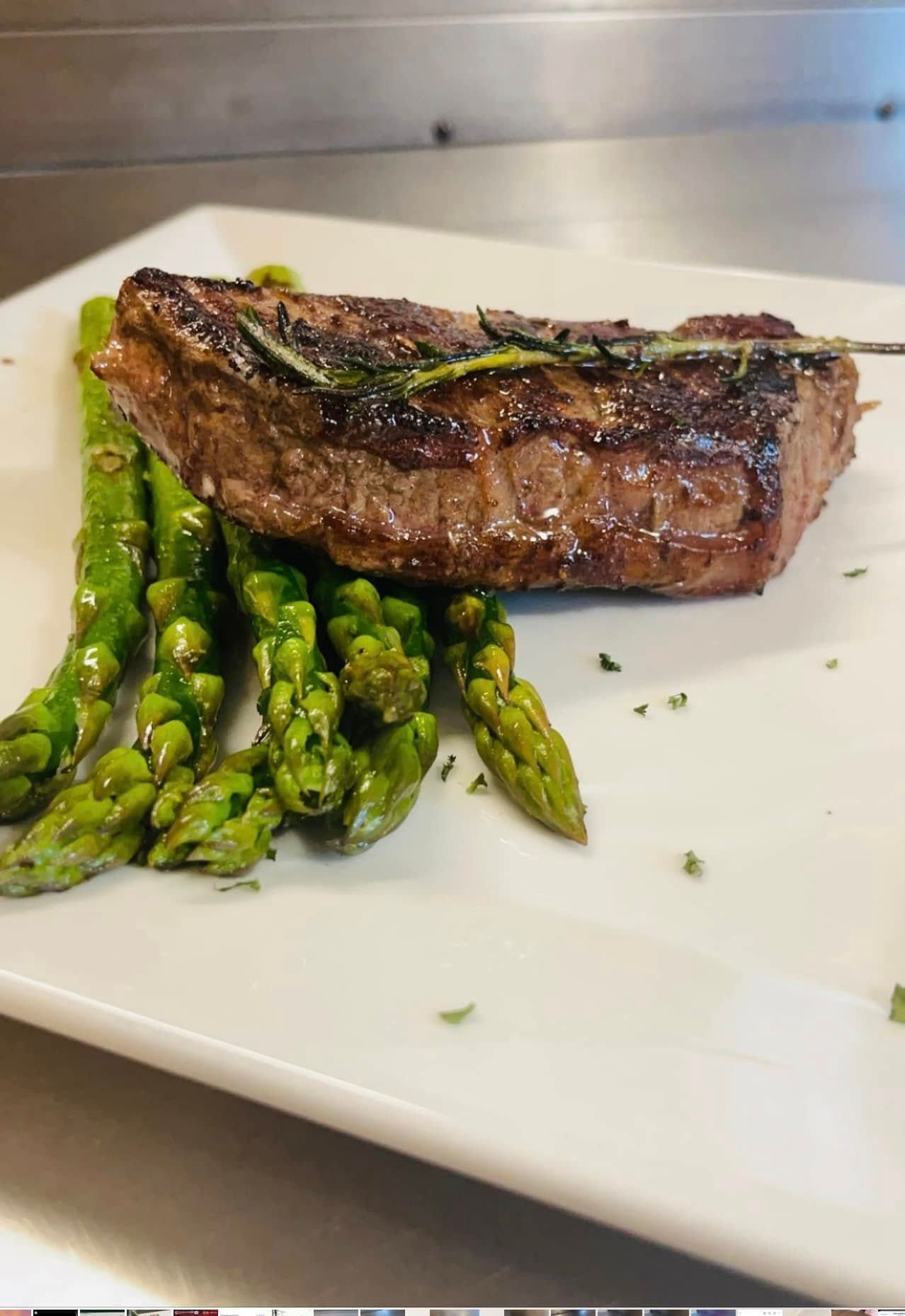 Grilled steak and asparagus on a white plate, garnished with herbs.