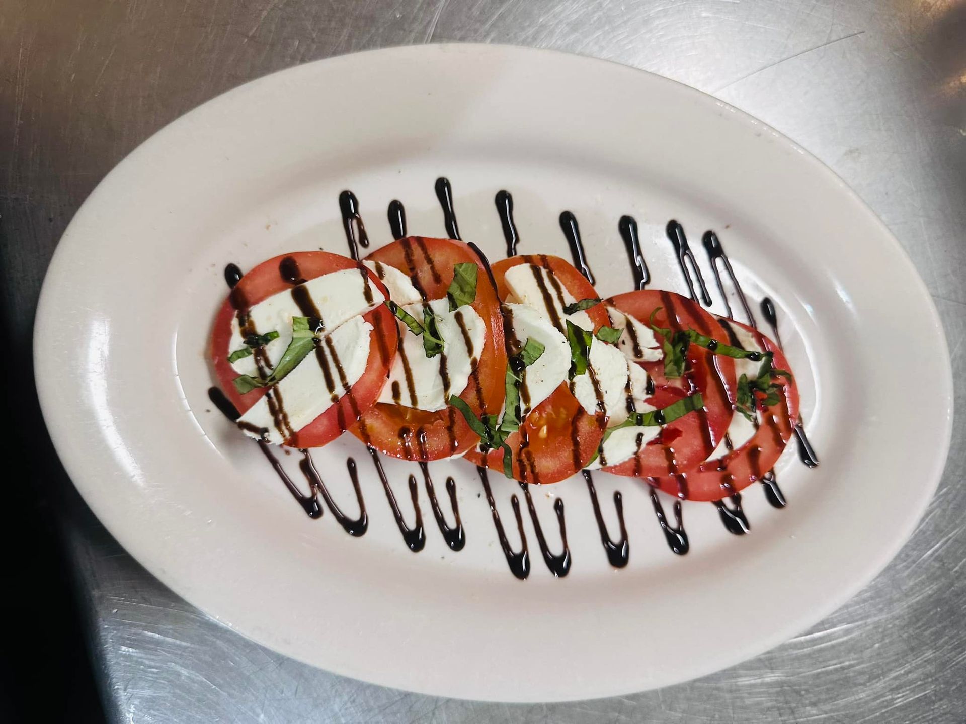 Caprese salad on a white oval plate with balsamic glaze and fresh basil.