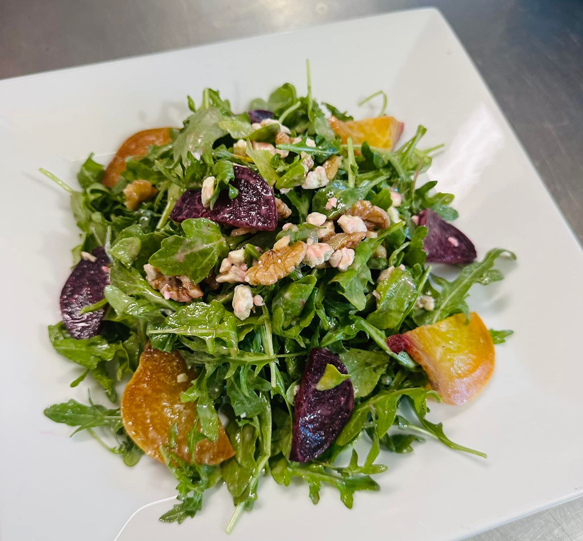 Arugula salad with beets, walnuts, and goat cheese on a white square plate.