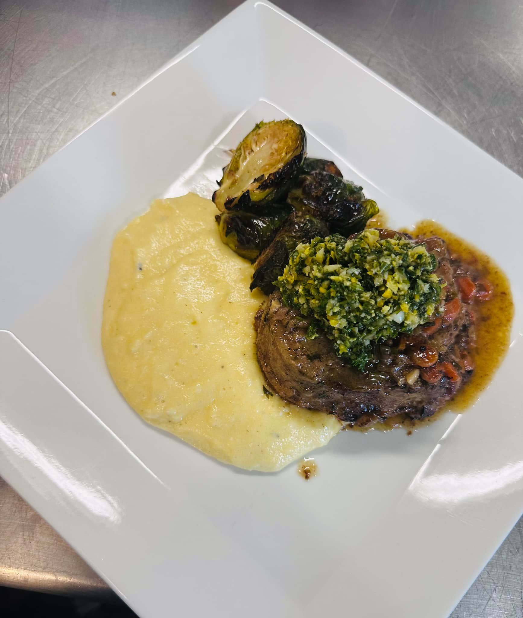 Steak with polenta, roasted Brussels sprouts, and sauce, plated on white square plate.