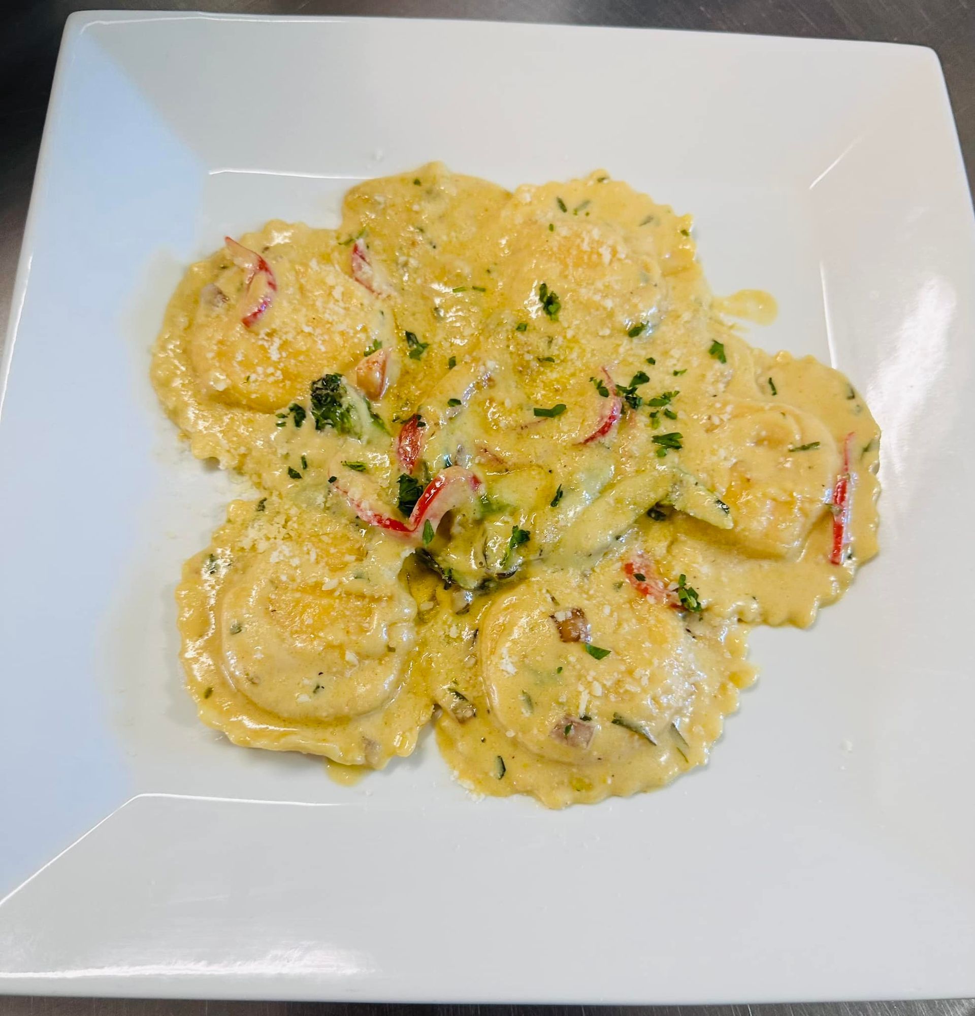 Round ravioli in creamy sauce, garnished with red peppers and herbs, on a white square plate.