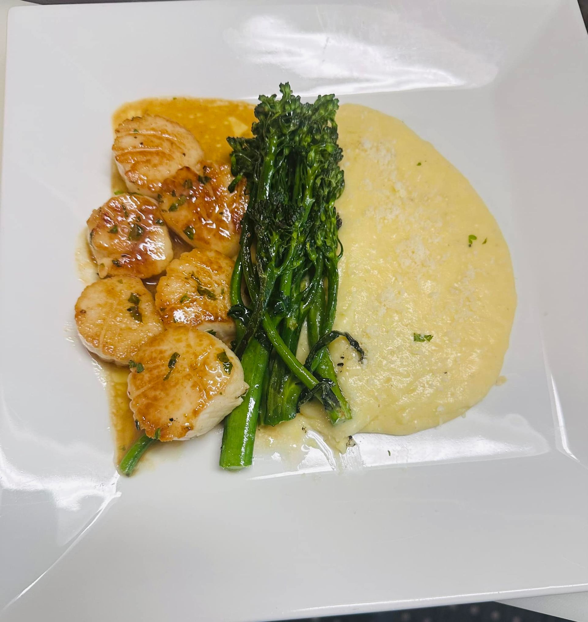Seared scallops with sauce, broccolini, and creamy polenta on a white plate.