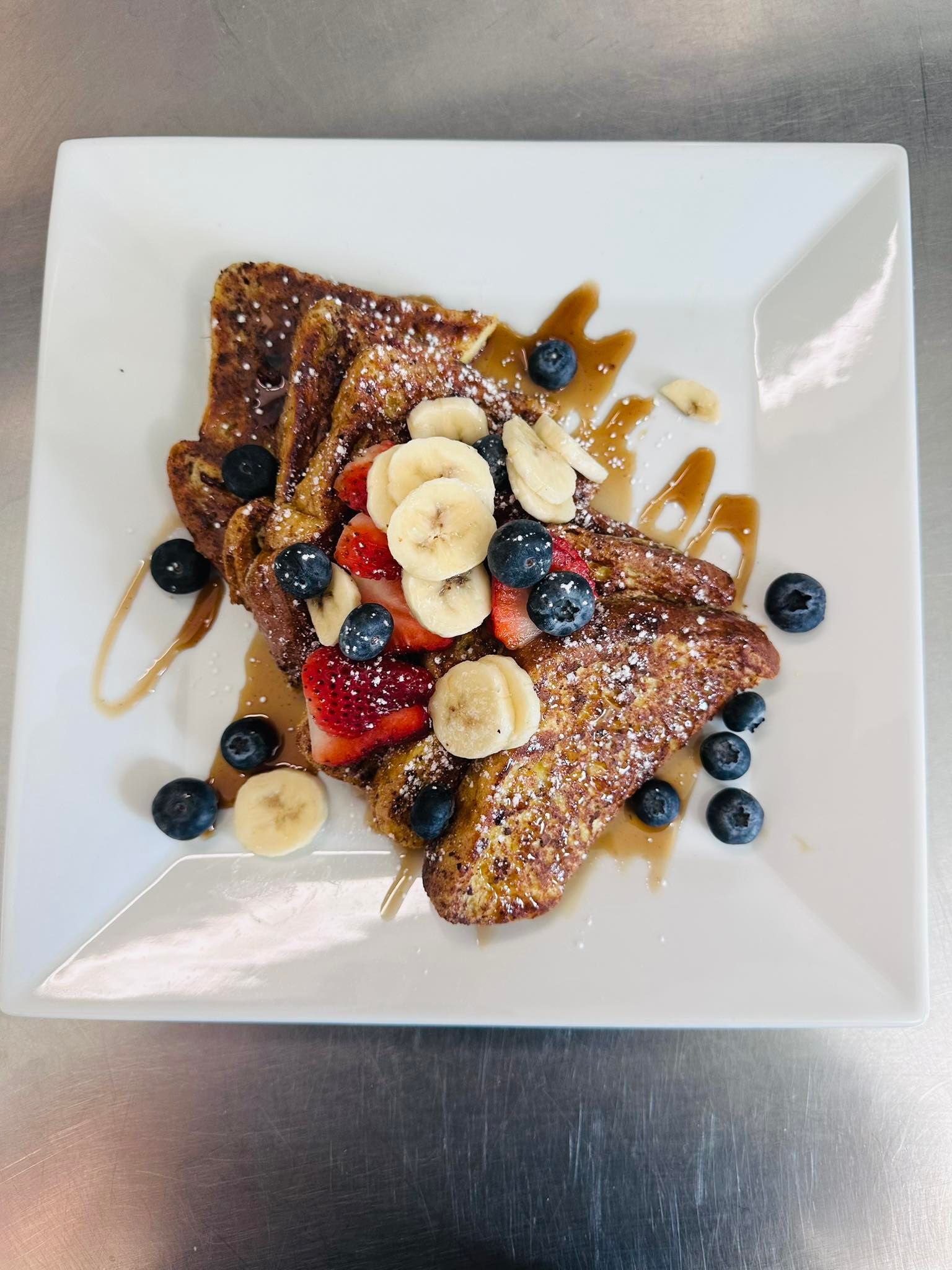 French toast topped with berries, banana slices, and syrup on a white plate.