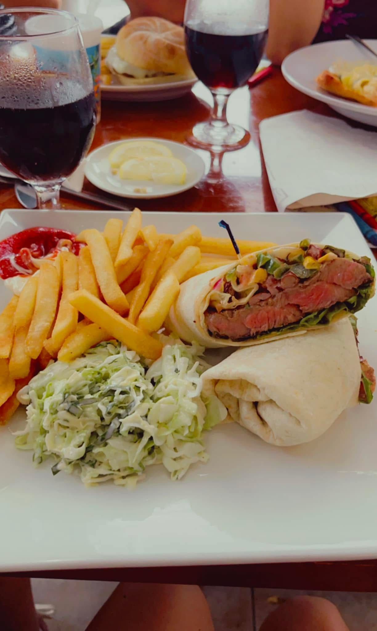 Plate with a burger wrap, fries, coleslaw, and dipping sauces with drinks in a restaurant.
