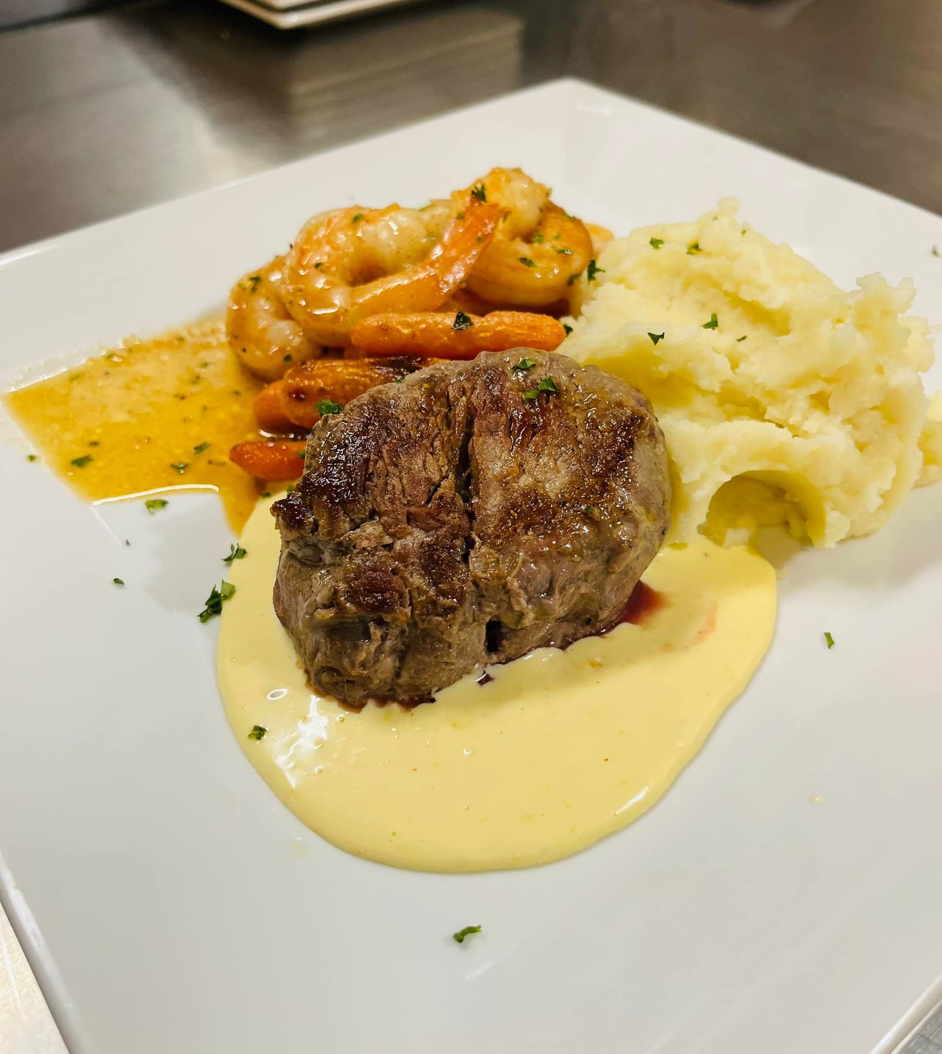 Steak, shrimp with sauce, and mashed potatoes on a white plate.