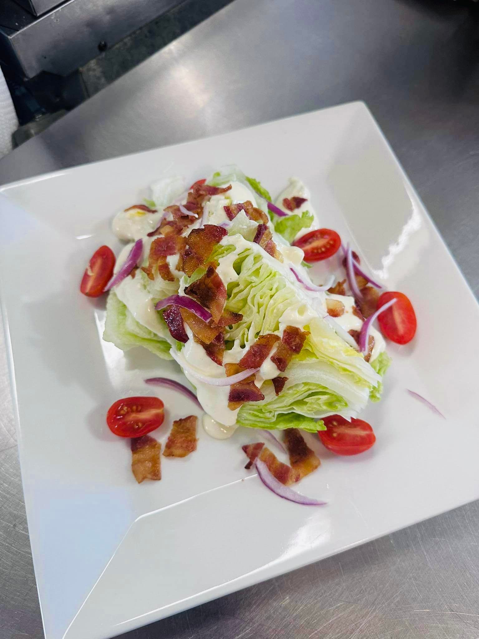 Wedge salad on white plate; lettuce, bacon, tomatoes, red onion, and dressing.