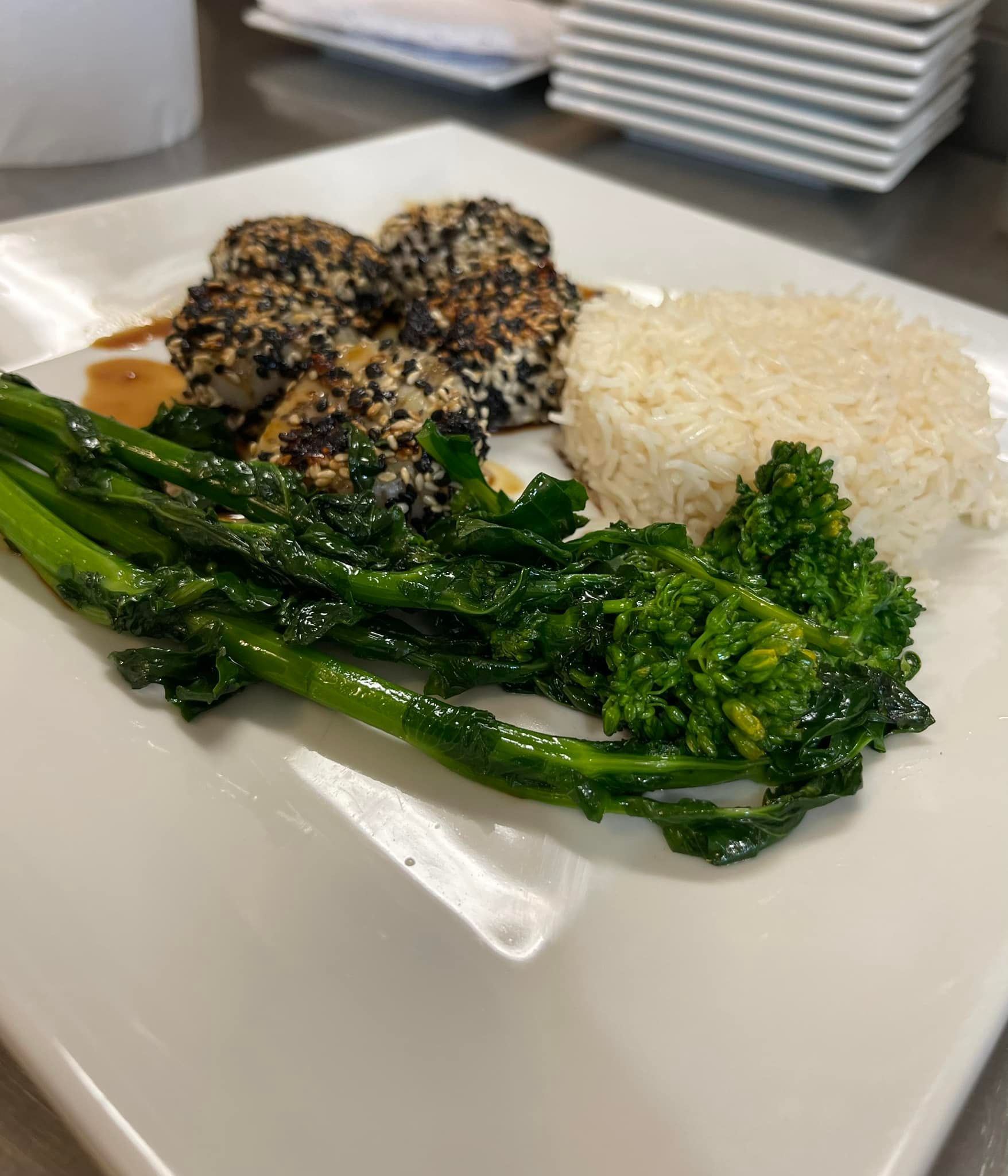 Sesame-crusted fish with rice and sauteed broccolini on a white plate.