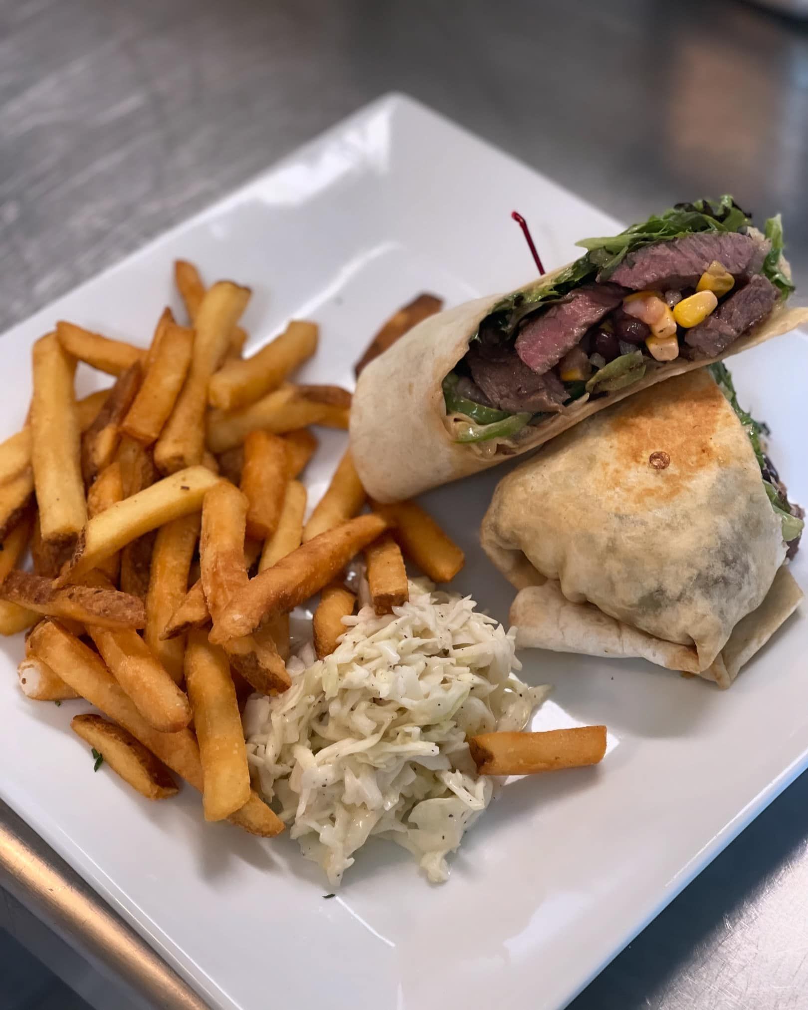 Steak wrap with fries and coleslaw on a white plate.