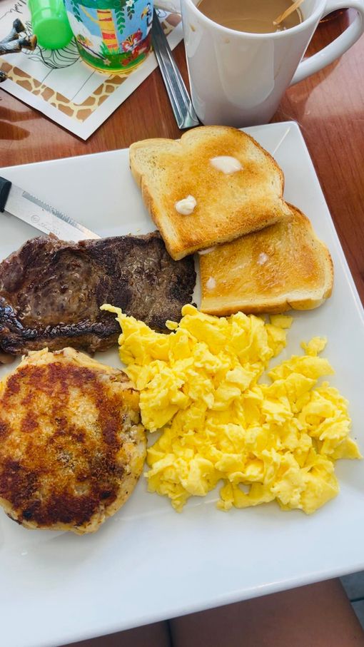 Breakfast plate with steak, toast, eggs, and a patty, coffee in background.