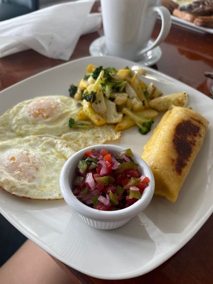 Breakfast plate: two sunny-side-up eggs, vegetable medley, a folded tortilla, and a salsa-filled bowl.