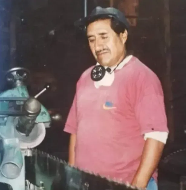 Hombre con camisa rosa de pie junto a una máquina de metal en un taller.