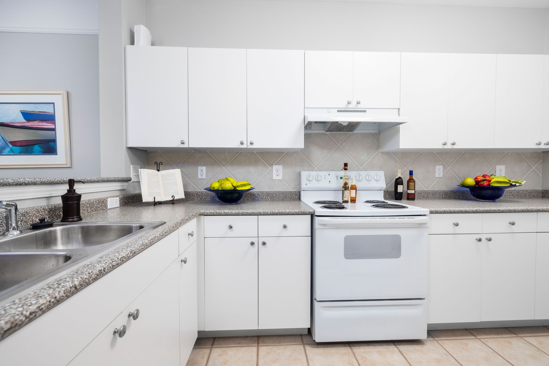 A kitchen with white cabinets , a stove , a sink and a picture on the wall | The Grove at Oakbrook