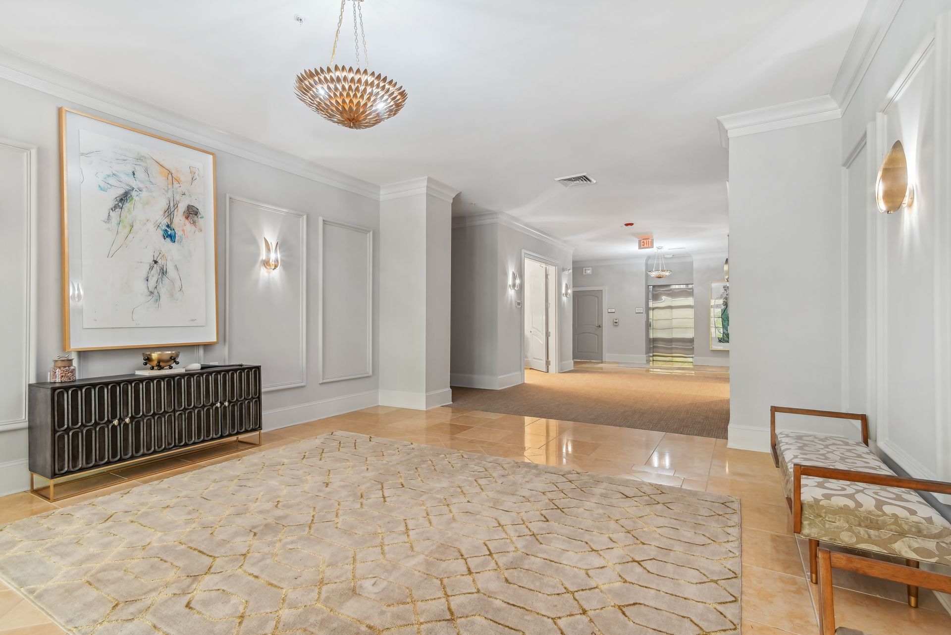 Elegant foyer with rug, artwork, chandelier, and a long hallway with light-colored walls and wood flooring.