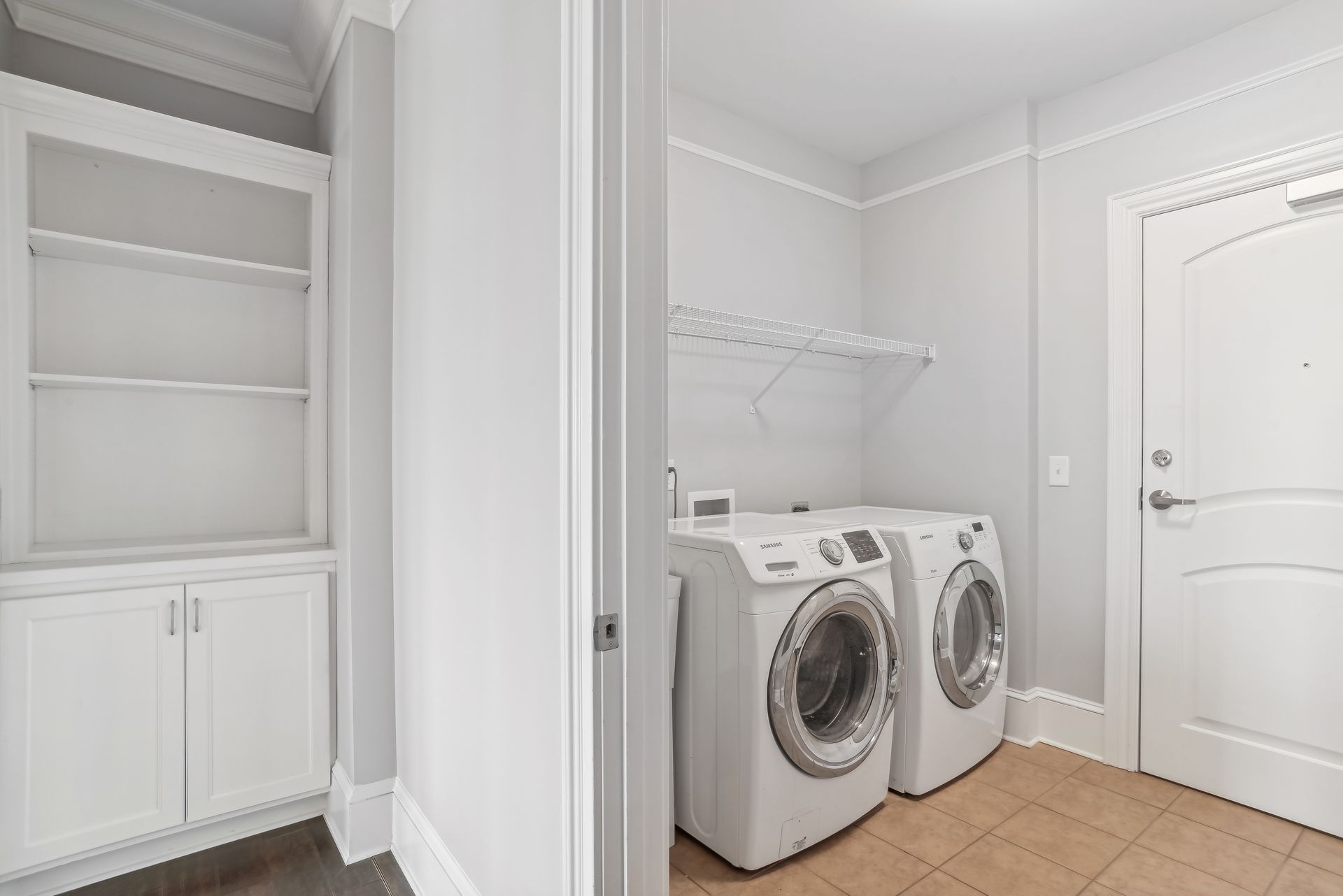 Laundry room with white washer and dryer, built-in shelves, and a closed door.