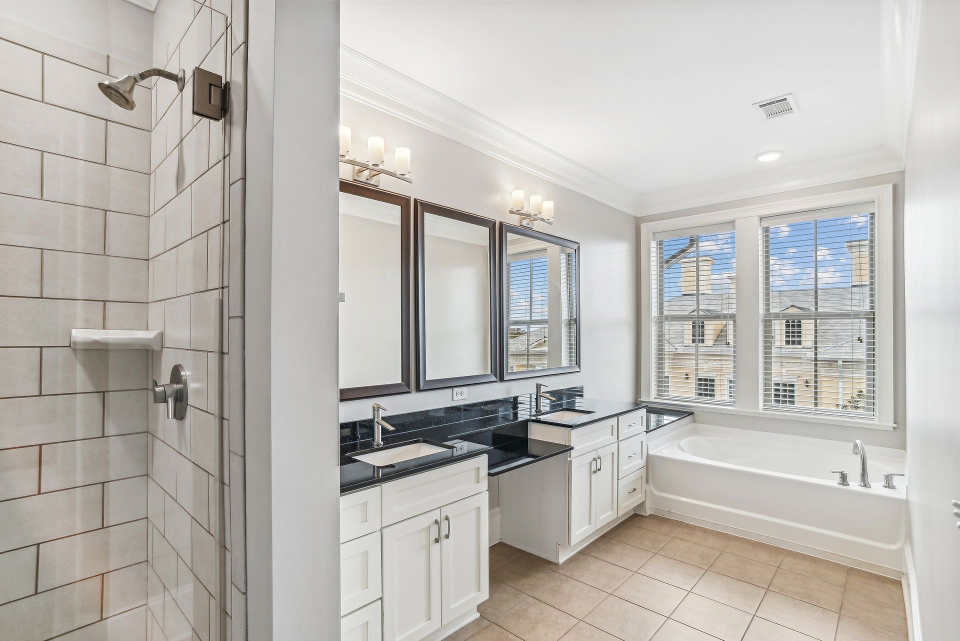 Bathroom with white tile shower, double vanity, bathtub, and large window.