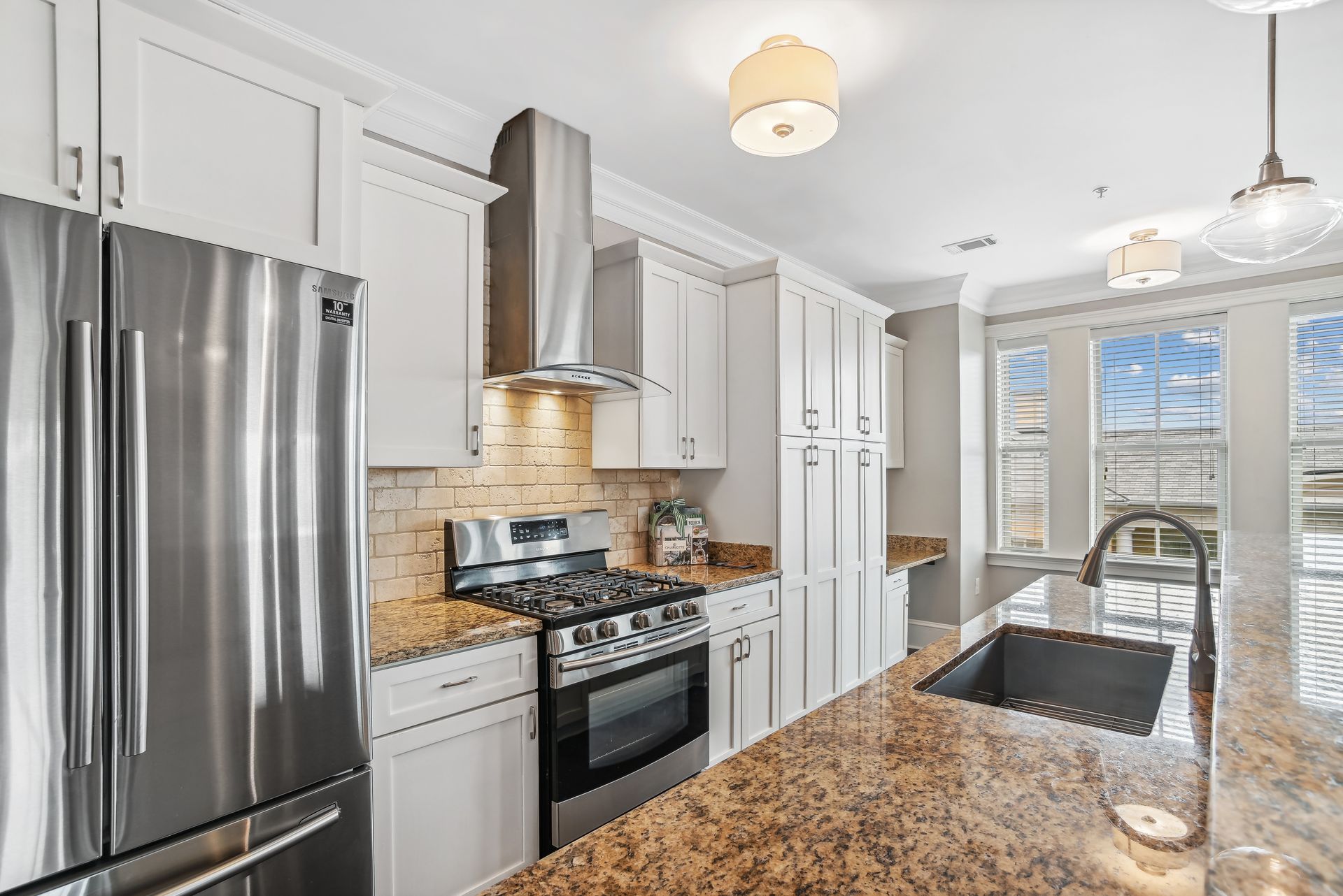 Stainless steel kitchen with white cabinets, granite countertops, and a window with natural light.