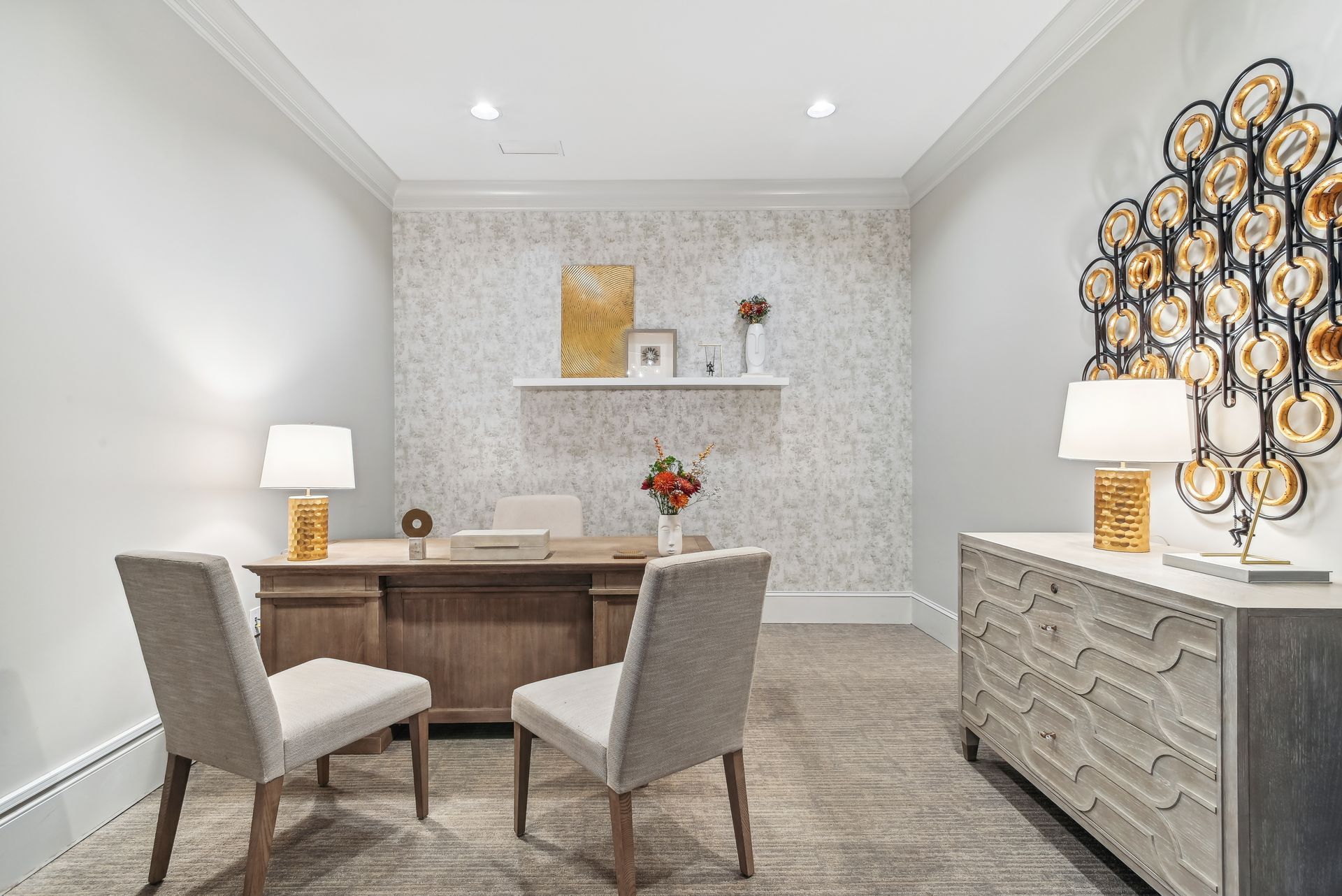 Office with desk, chairs, artwork, lamps, and neutral-colored walls and carpet.