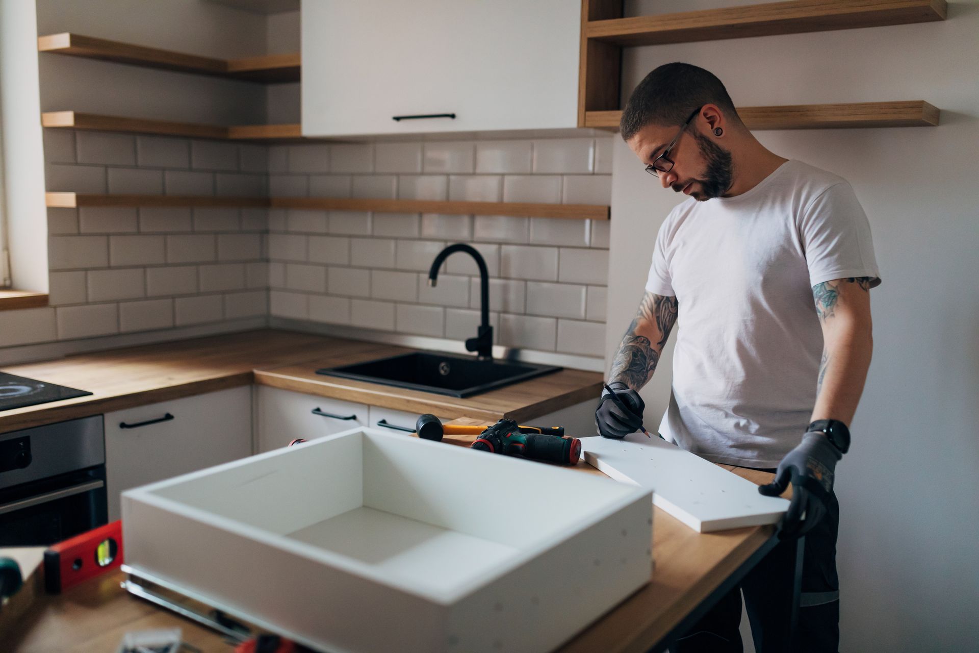 Man with tattoos working in a kitchen, assembling a cabinet.
