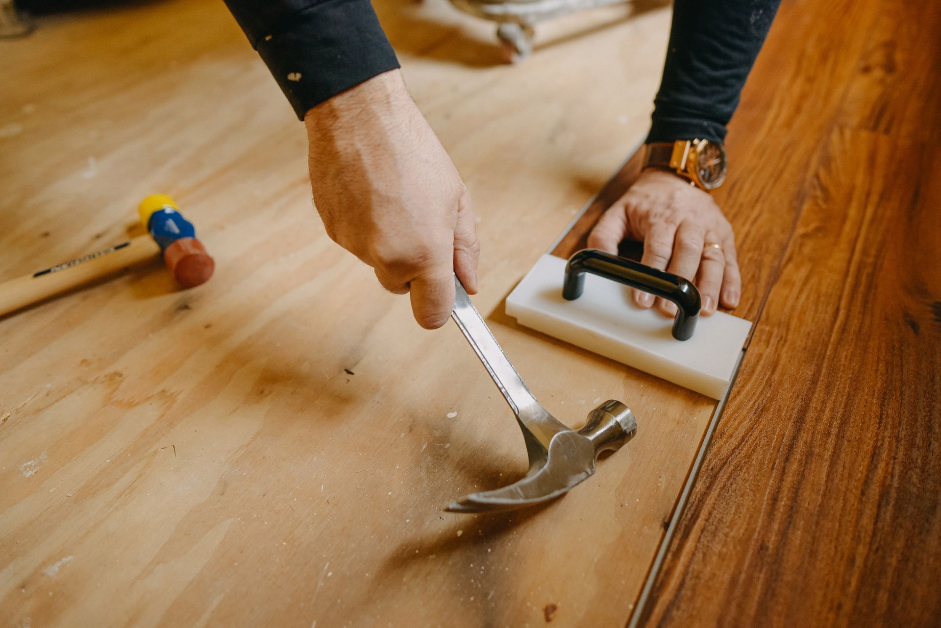Person installing laminate flooring, hammering a piece with a hammer and tapper.