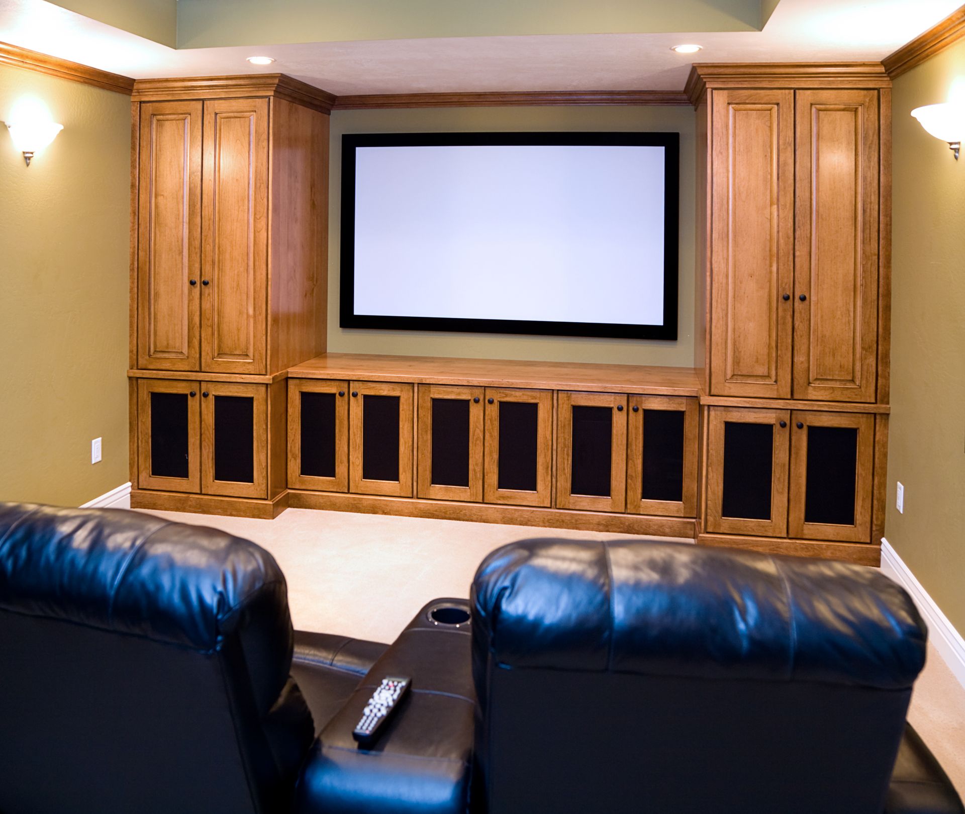 Home theater with screen, speakers, cabinetry, and two black leather recliners with remote.