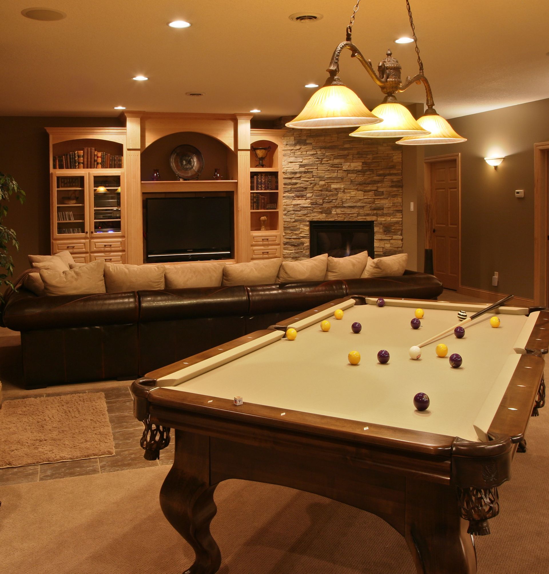 Pool table in a finished basement with a large sectional sofa and fireplace.
