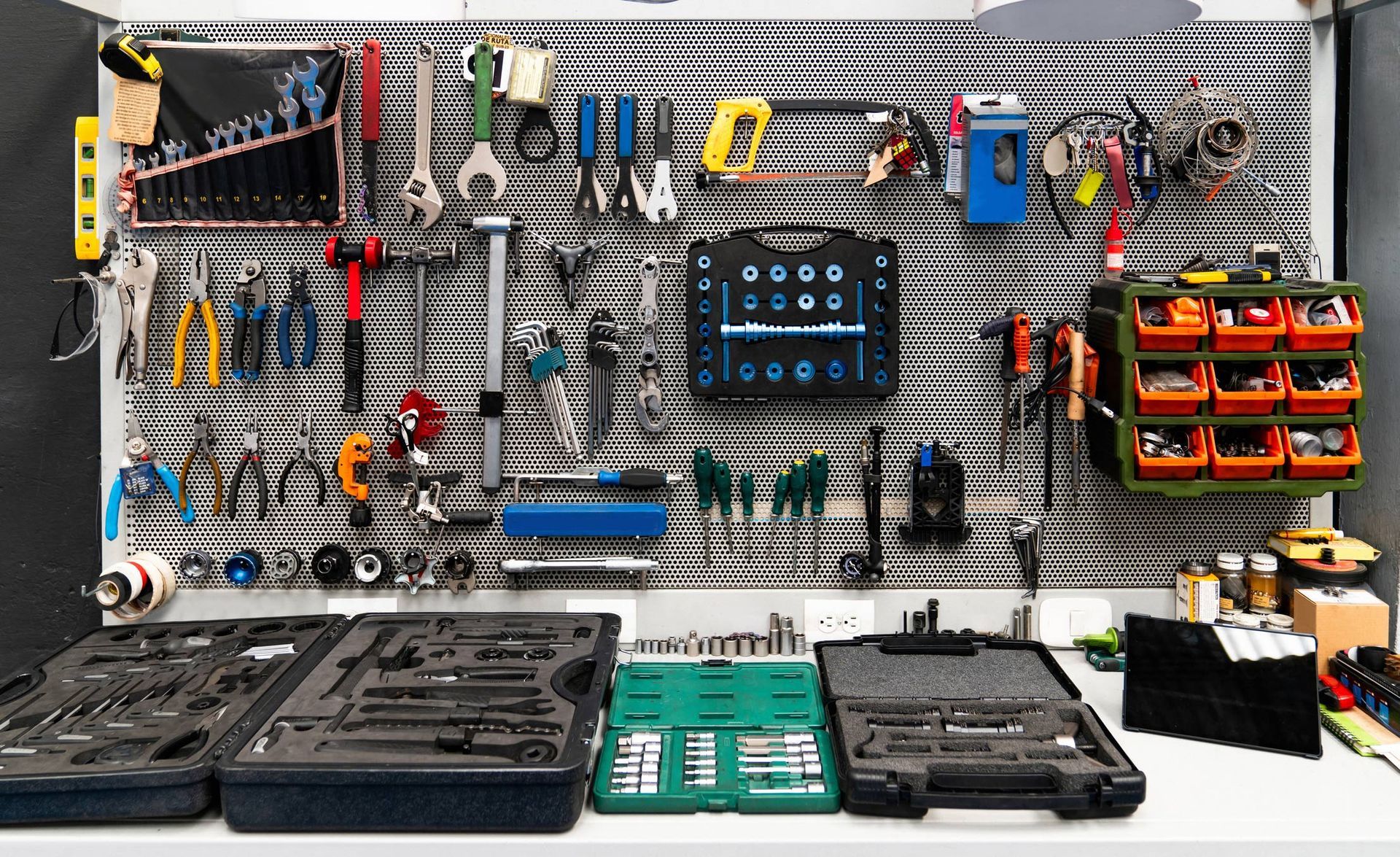 Tools organized on a pegboard, including wrenches, pliers, and toolboxes in a workshop setting.