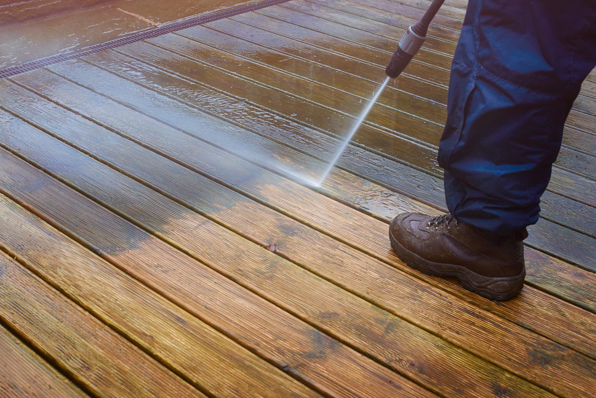 A man is using a high pressure washer to clean a wooden deck.
