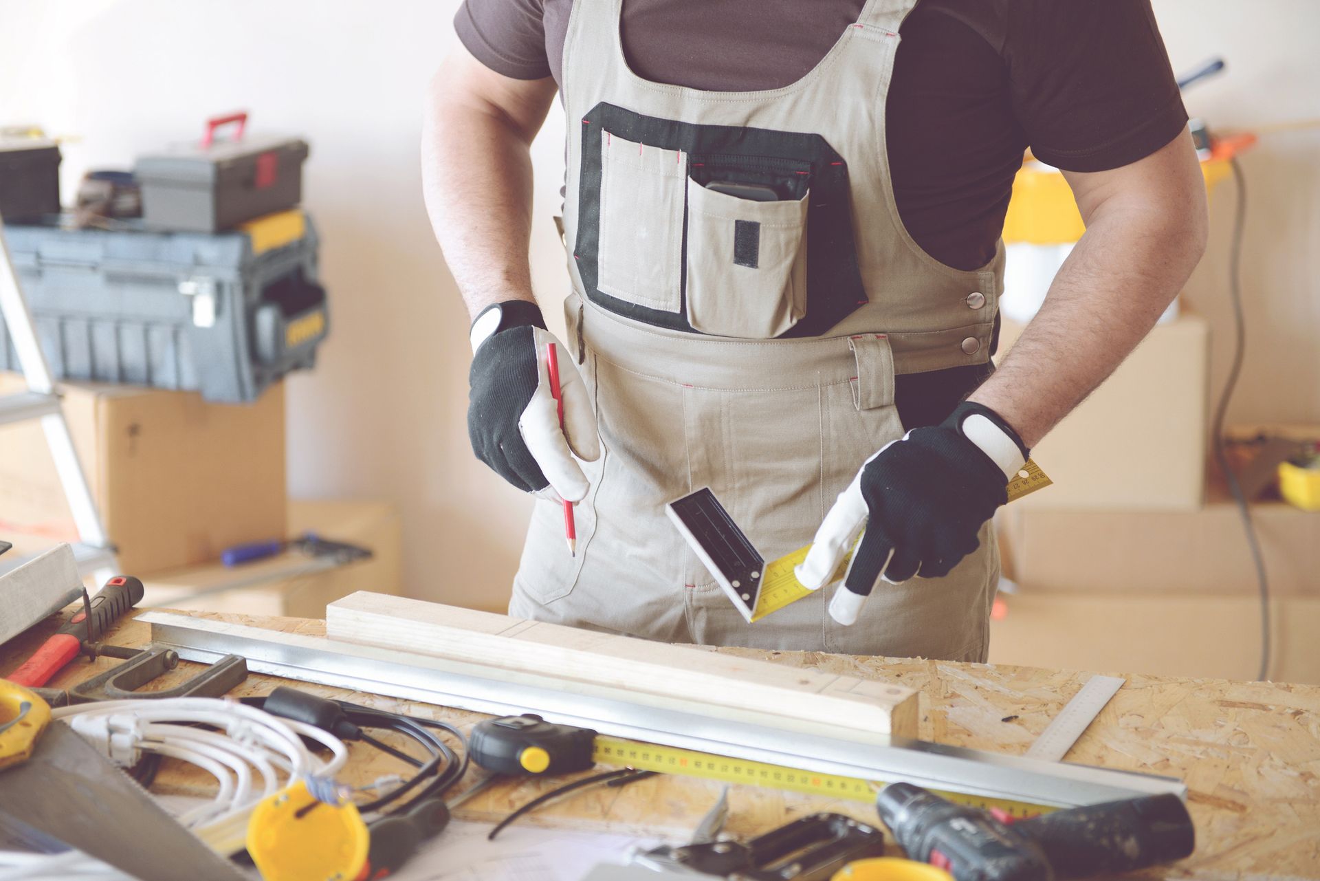 Carpenter using a square and pencil to measure wood on a workbench with tools in a workshop.