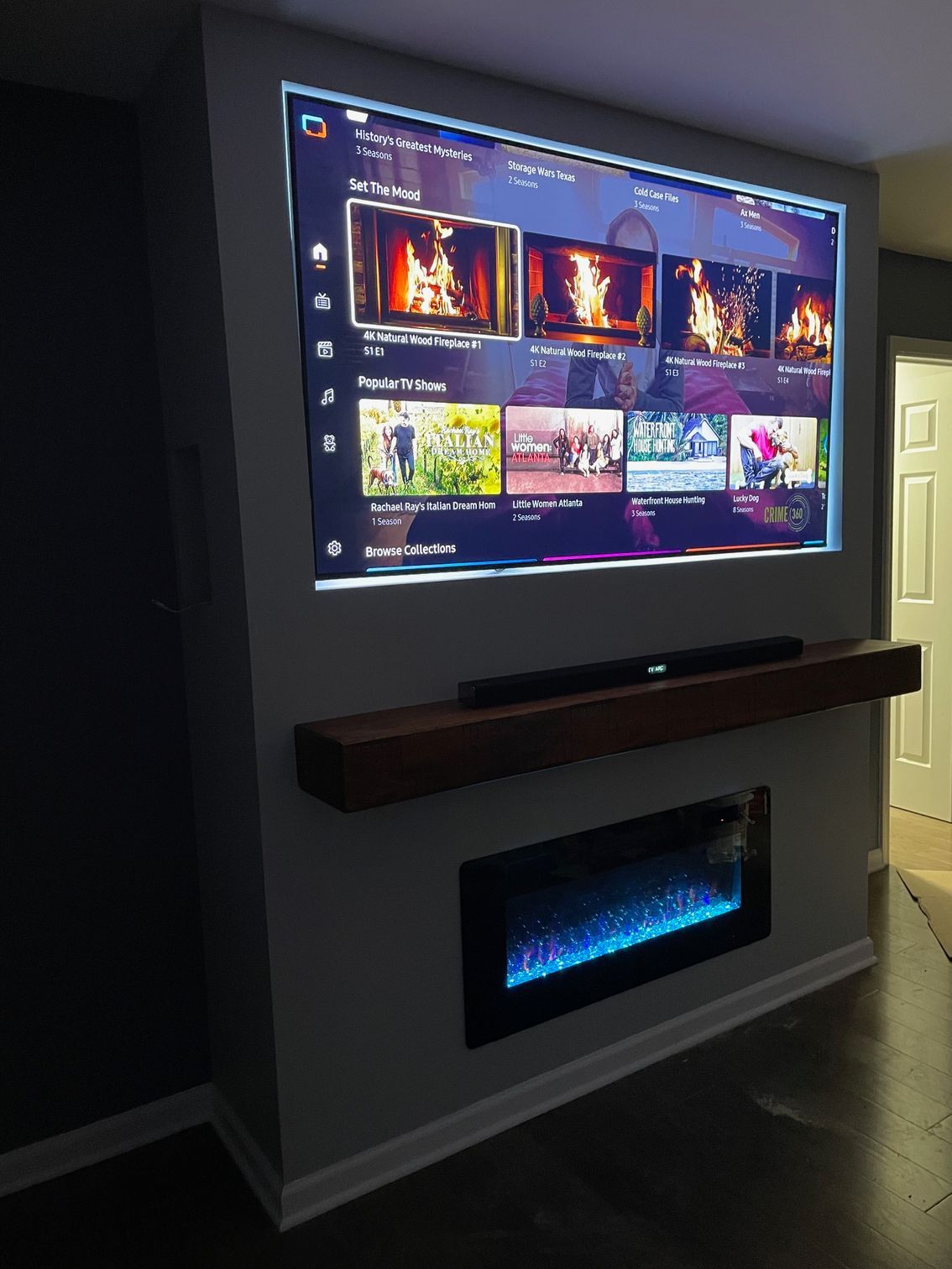 TV and electric fireplace built into a gray wall, with a wooden mantel.